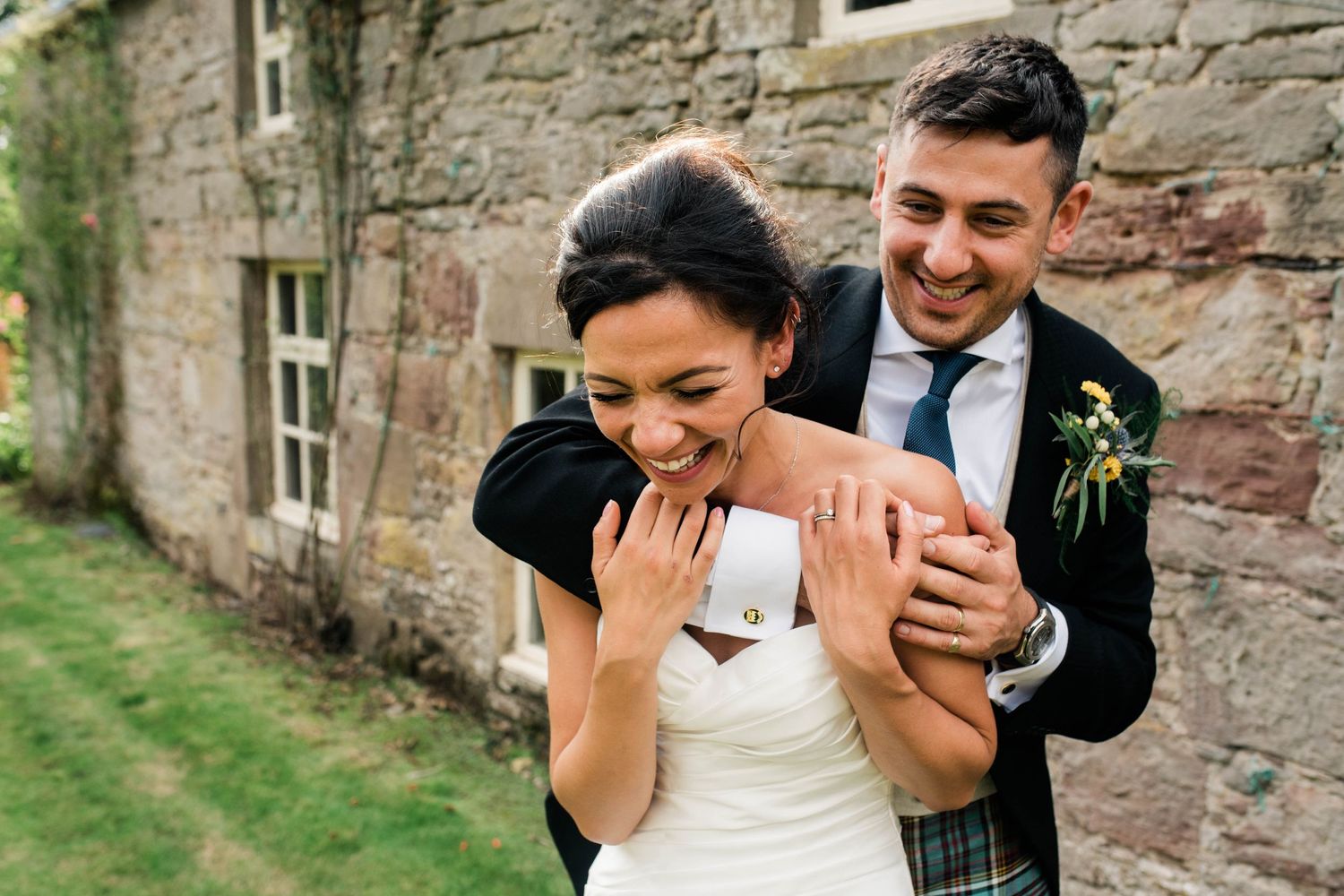A joyful moment shared between newlyweds against a rustic stone wall.