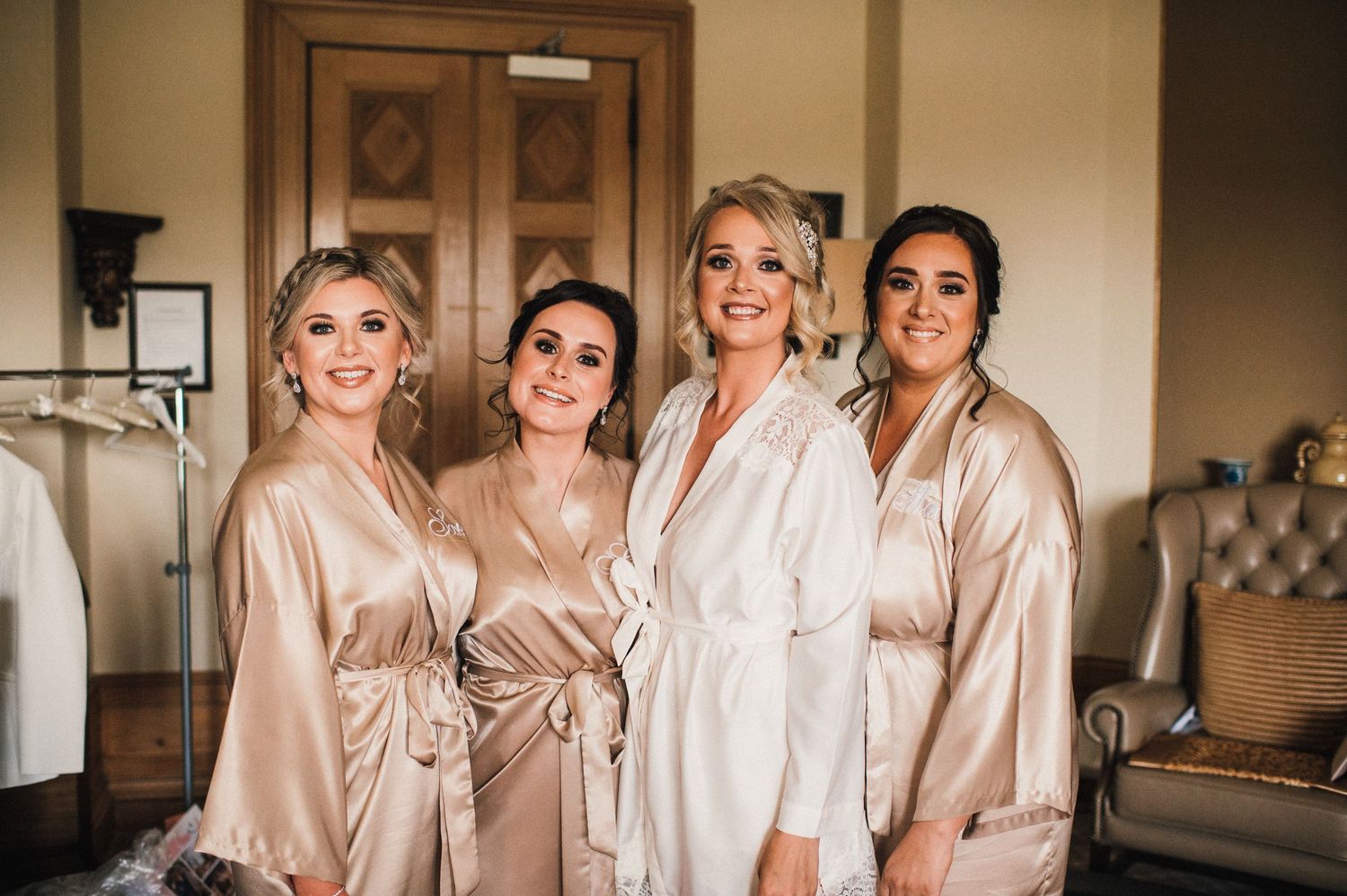 Bridesmaids in champagne colored robes pose together during wedding preparations.