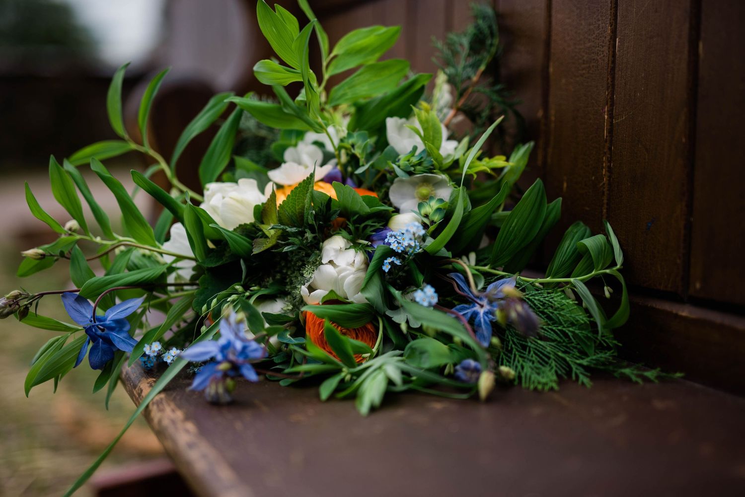 Fresh floral arrangement with blue and white flowers mixed with greenery on a wooden surface.