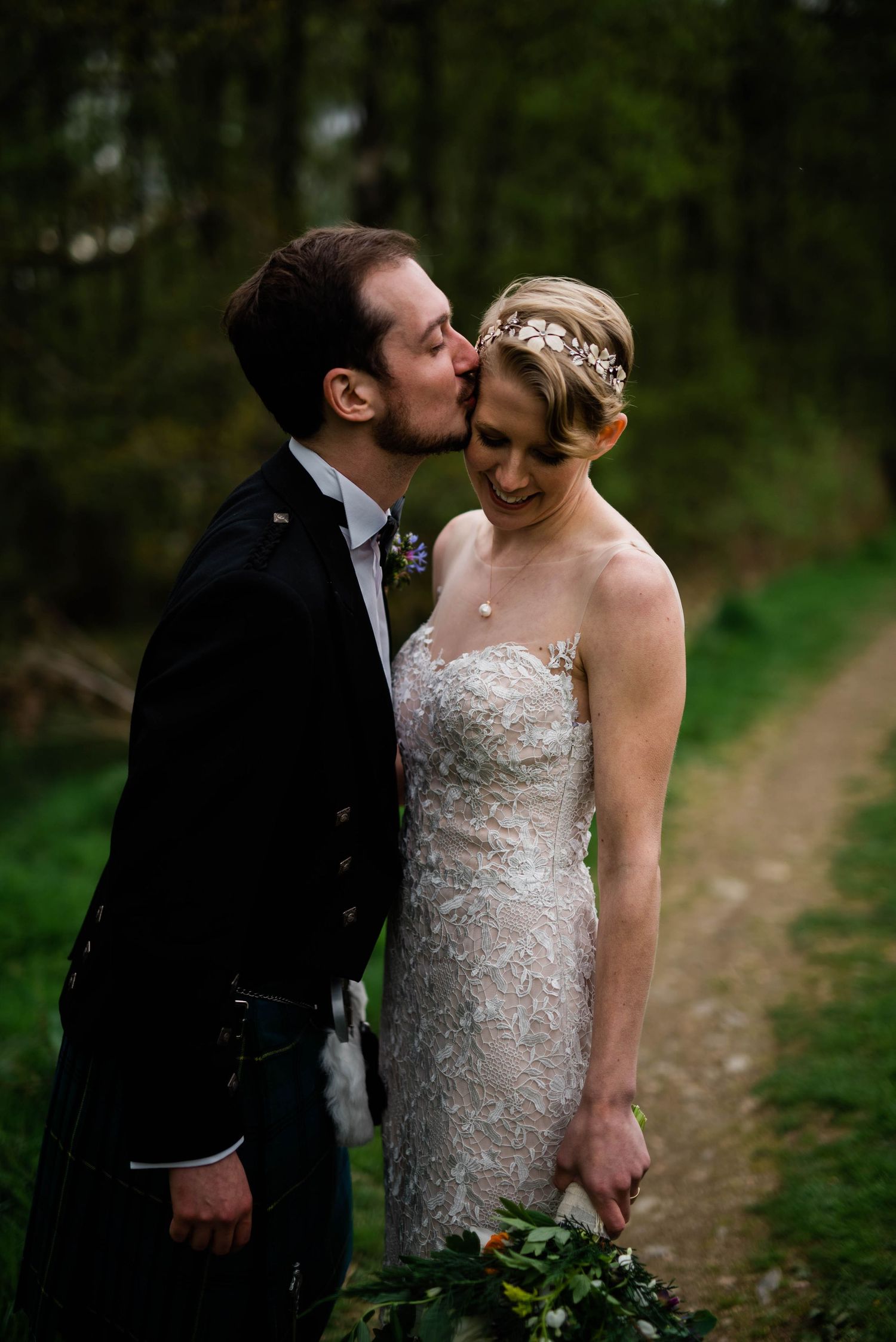 An intimate moment between a couple in wedding attire on a forest path.