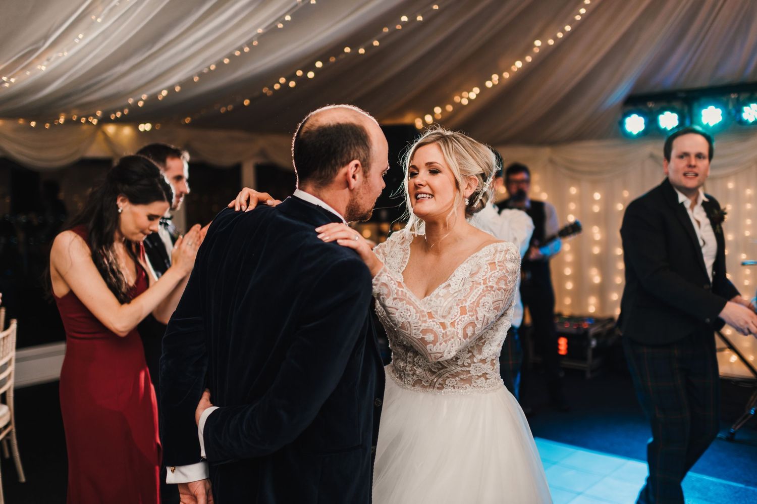 Couples dance together during an elegant wedding reception with twinkling lights and fabric draping overhead.