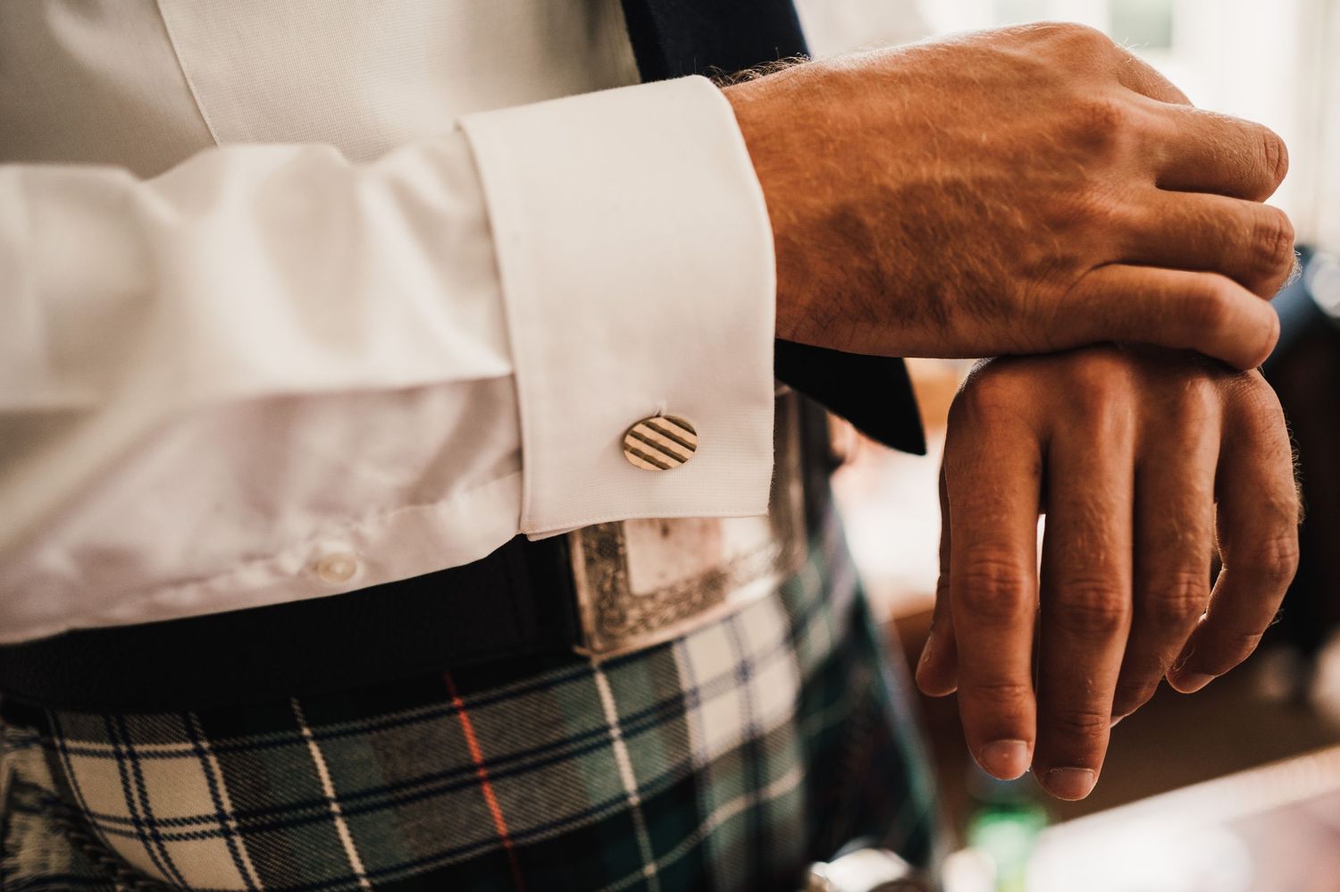 Close-up of a gold cufflink against a traditional tartan kilt pattern.