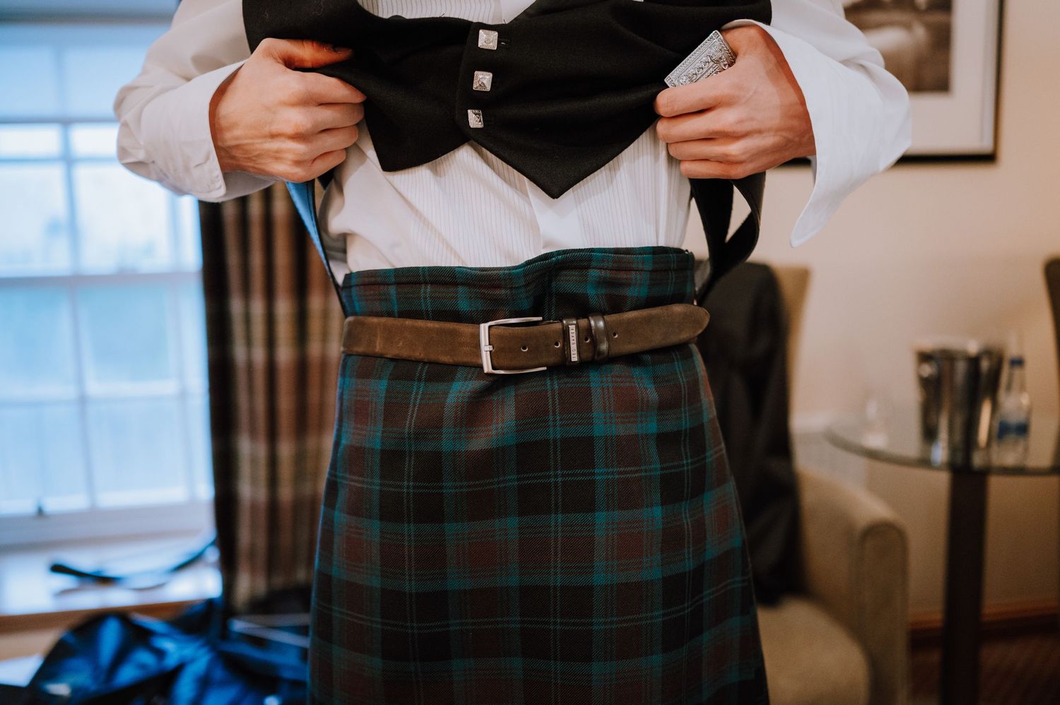 Close-up of traditional Scottish tartan kilt with black vest and leather belt.