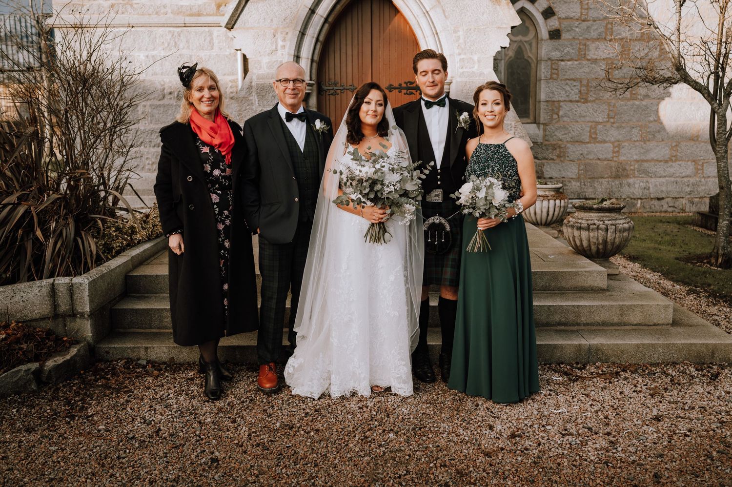 Wedding group portrait featuring traditional white dress and emerald green bridesmaid gown.