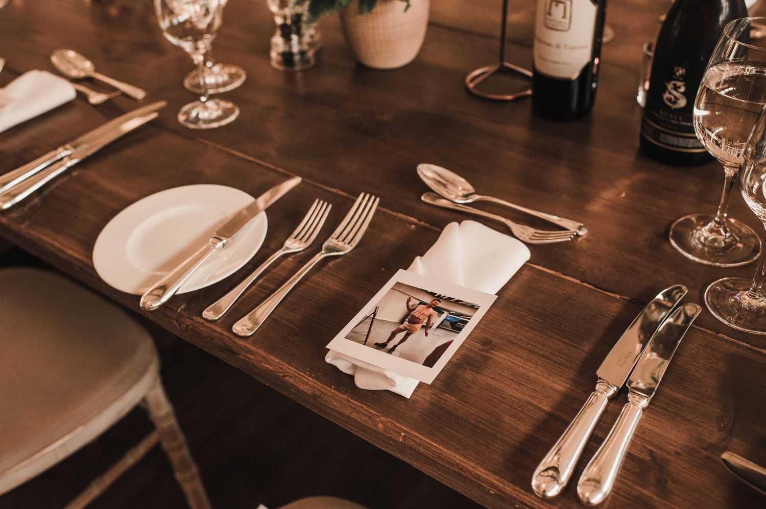 Formal place setting with silverware, plates and wine glasses on wooden table.