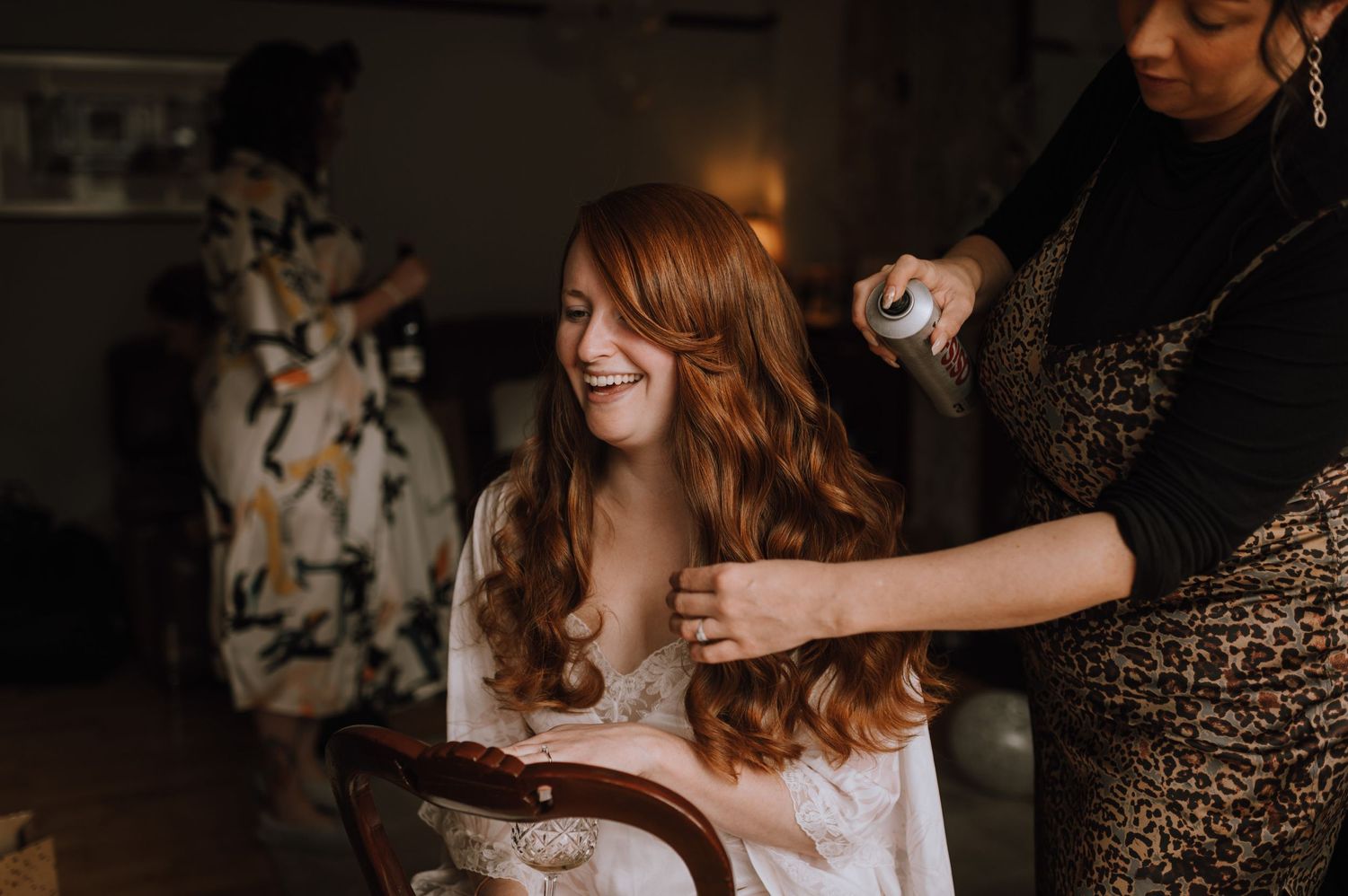 Bridal preparation scene with hairstyling in a dimly lit room.