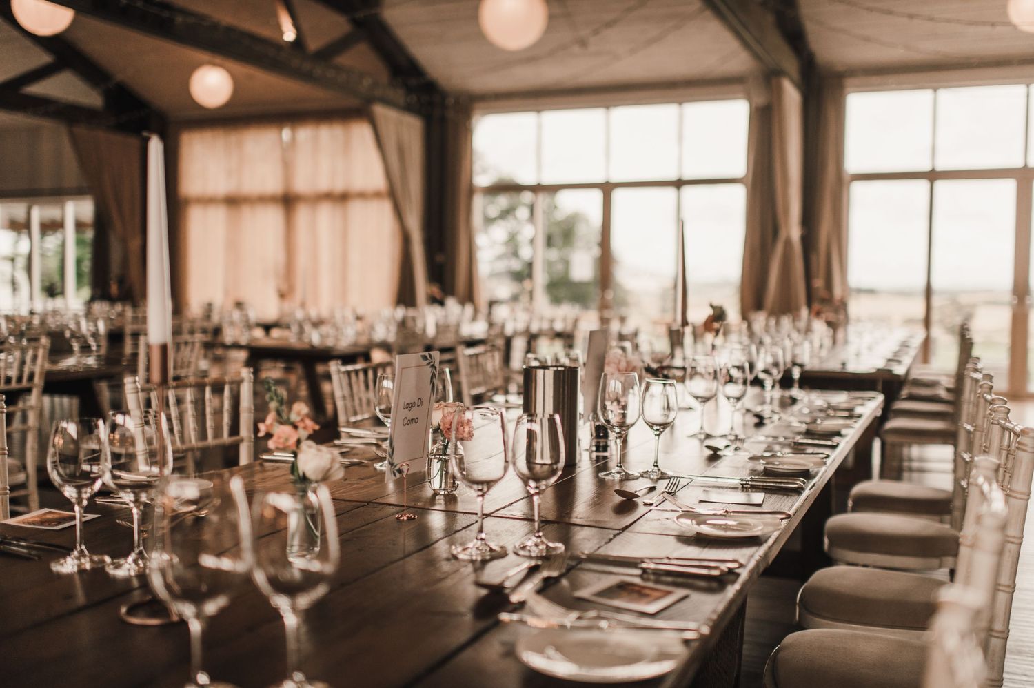 Elegant wedding reception table setup with wine glasses and place settings in rustic venue.