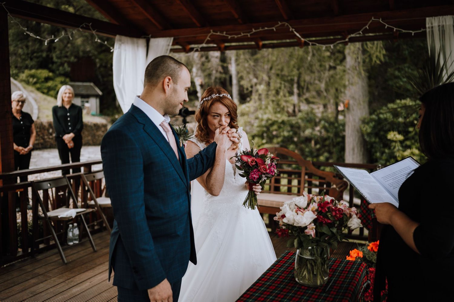 Bride laughs while holding bouquet next to groom during outdoor ceremony.