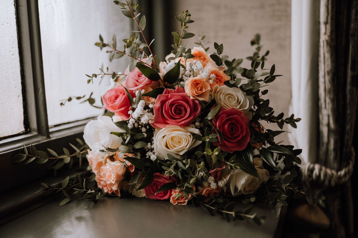 Romantic wedding bouquet with pink and cream roses near a window.