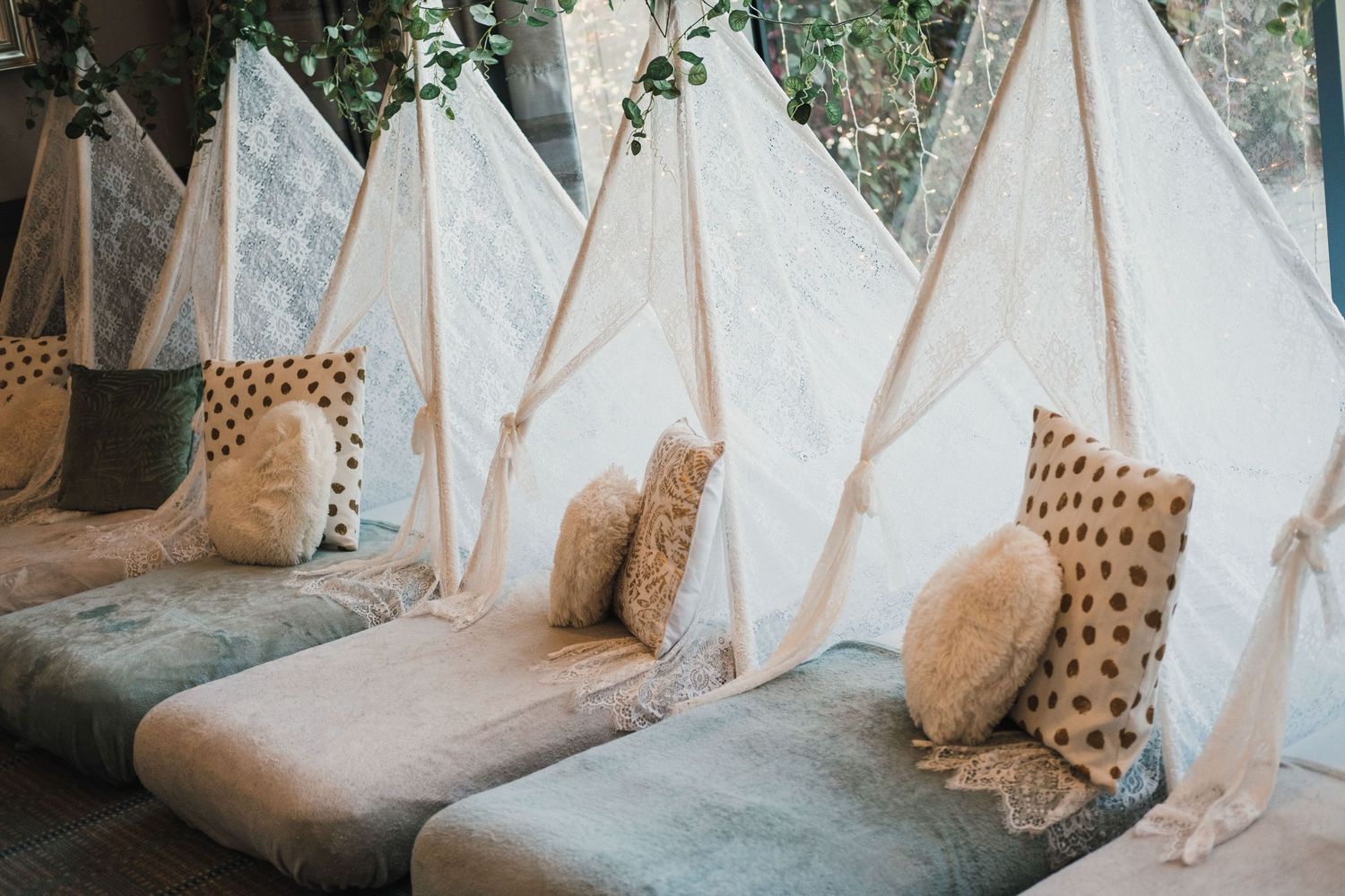 Bohemian lounge area with white teepee tents and patterned pillows for wedding guests.