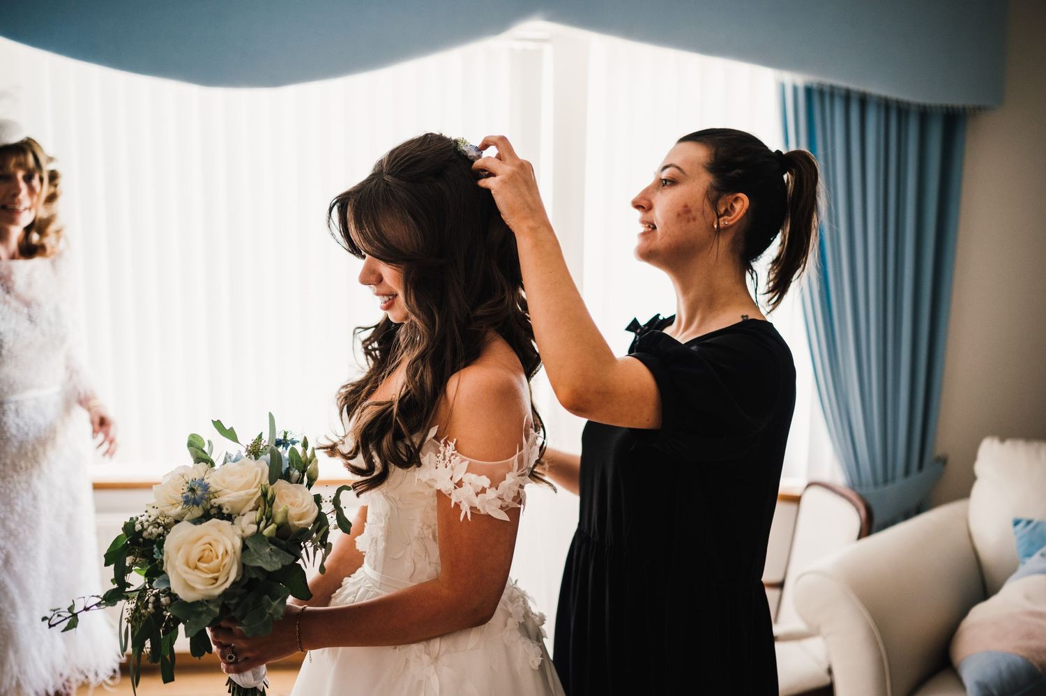 A stylist puts finishing touches on bridal hair preparations in a bright room.