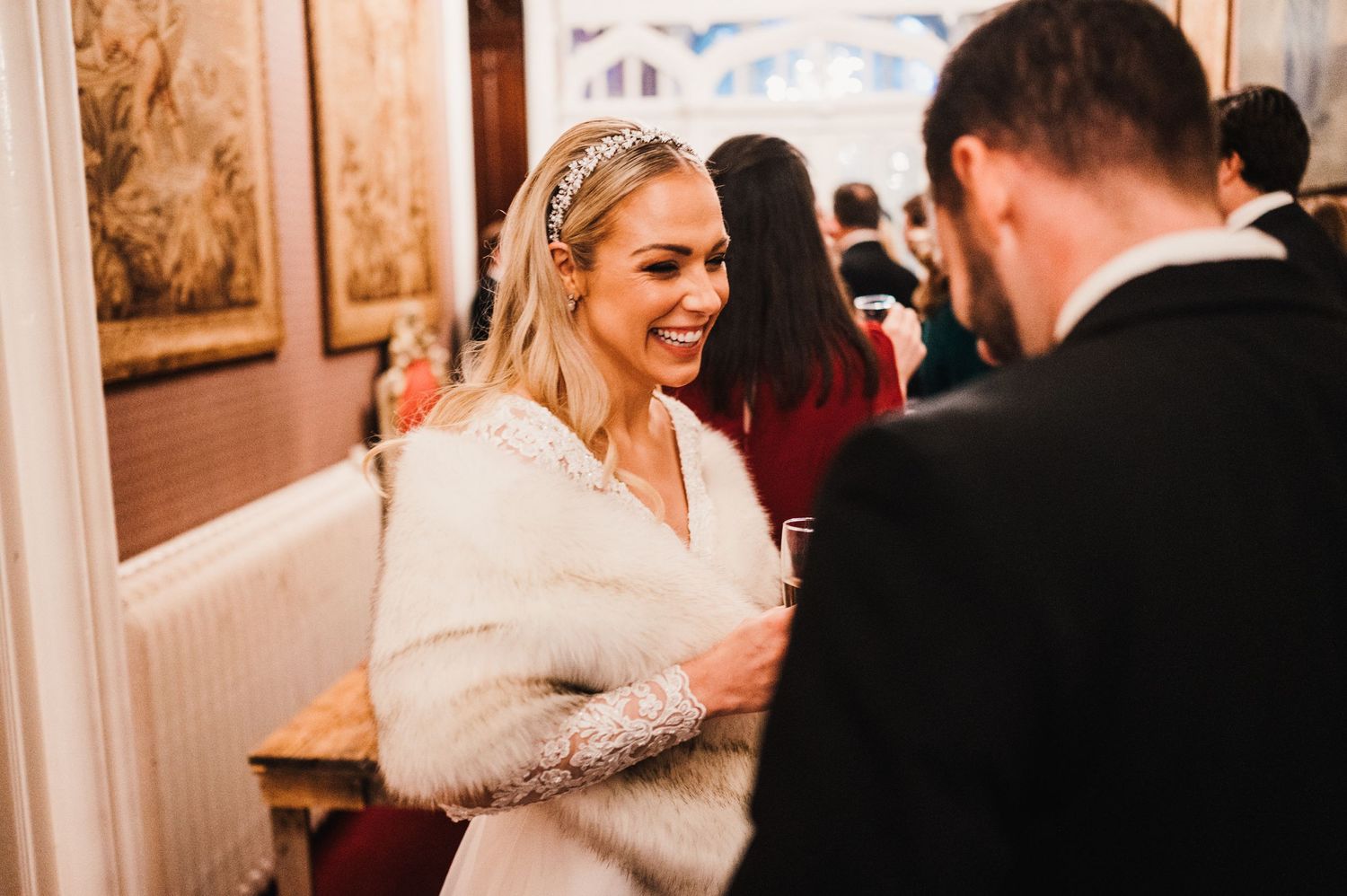 A bride wearing a white fur wrap smiles during an elegant indoor wedding reception.