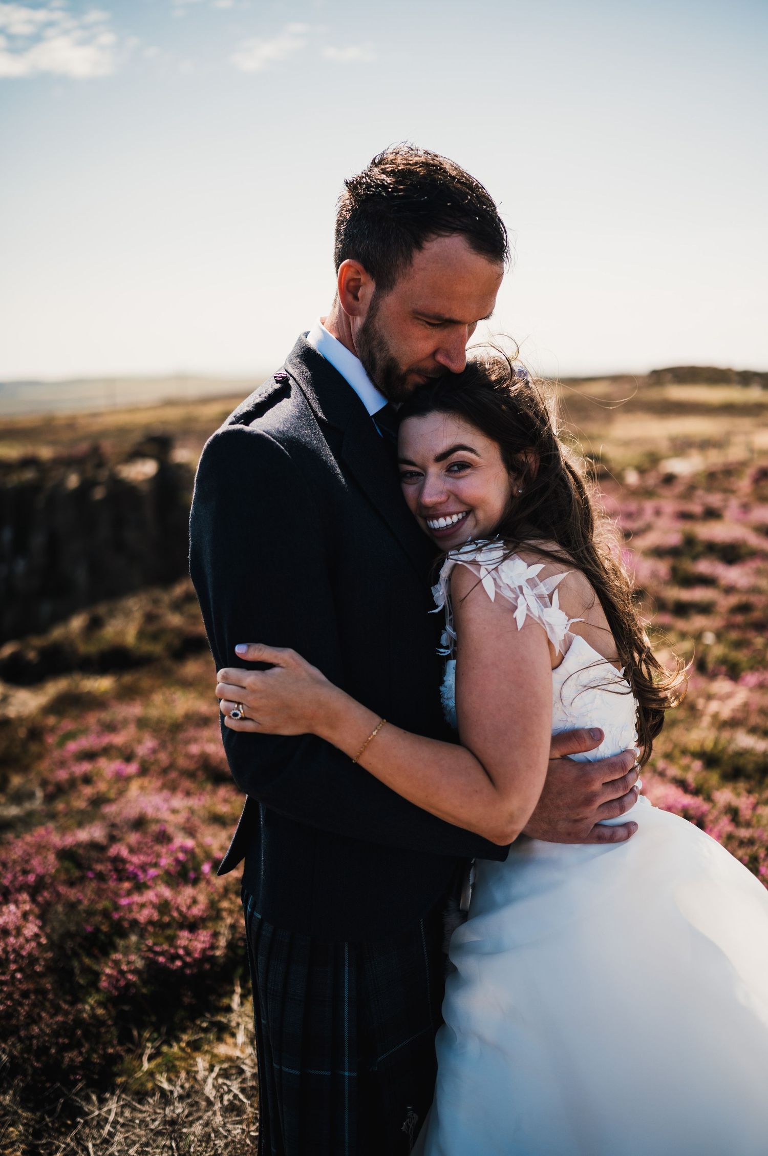 Couple shares intimate moment among purple heather on Scottish hillside.