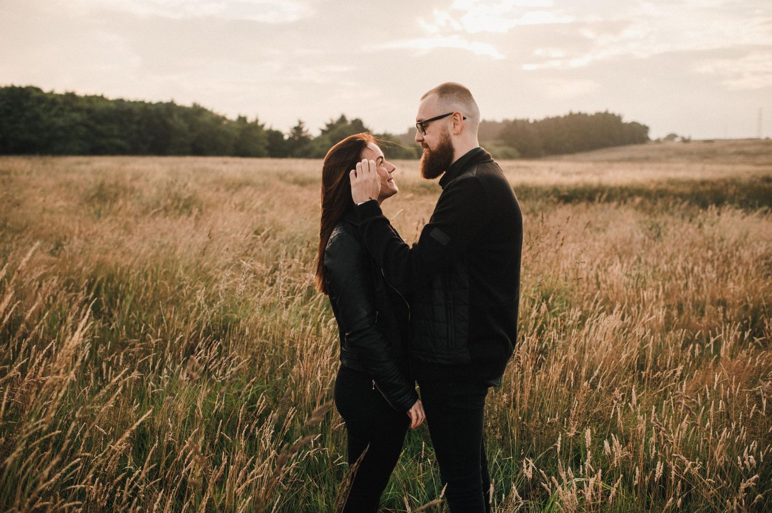 Two people share an intimate moment while standing in tall grass during golden hour.