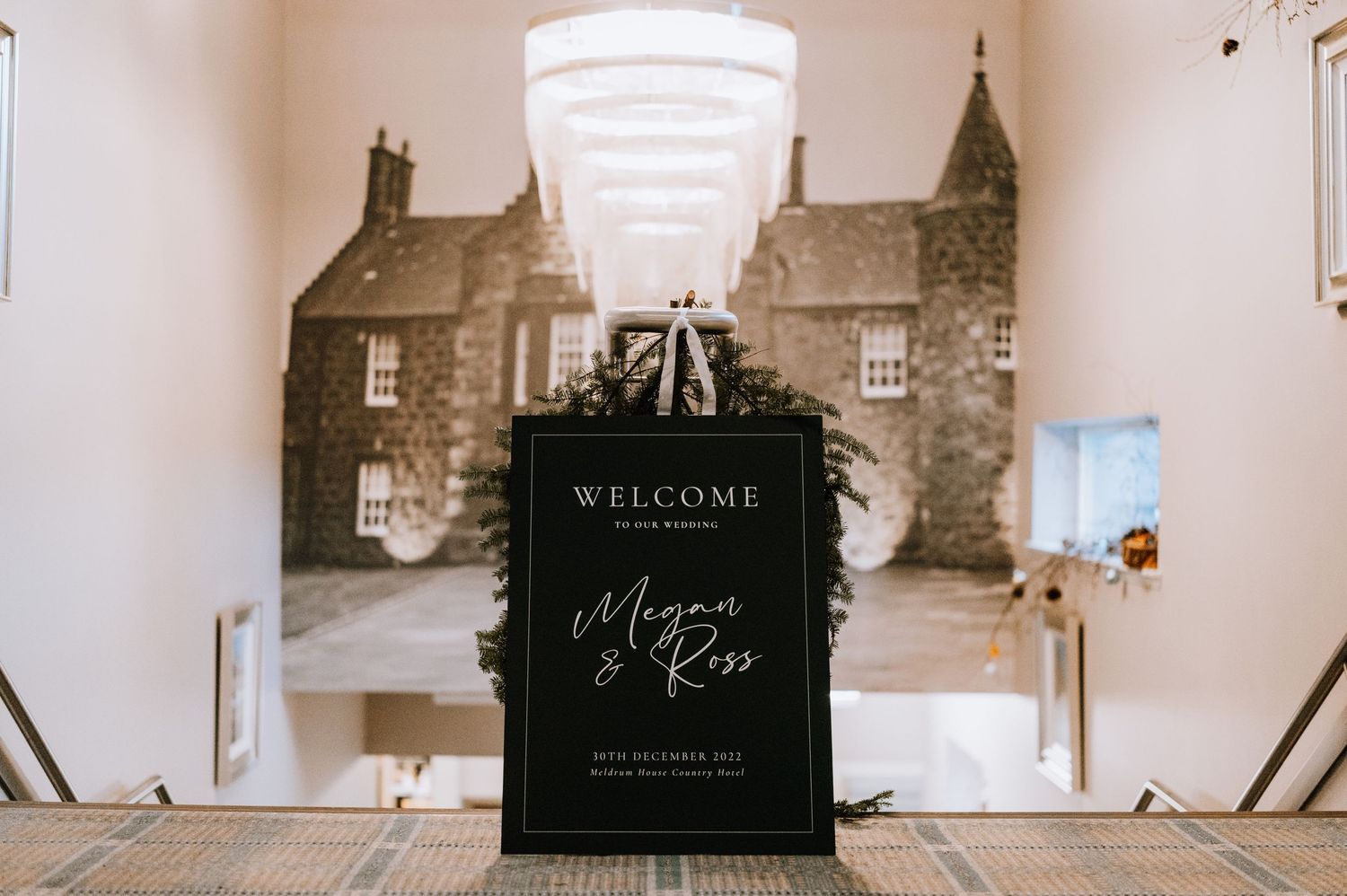 Black welcome sign with vintage building backdrop at wedding reception.