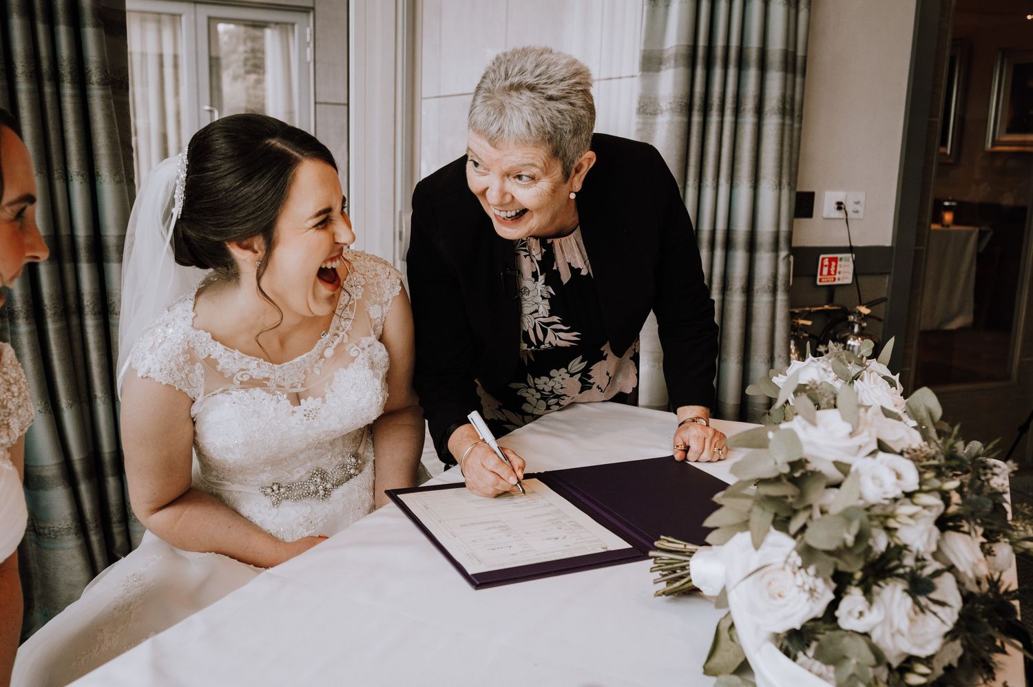 A bride in a beautiful lace gown signs paperwork during her wedding ceremony.