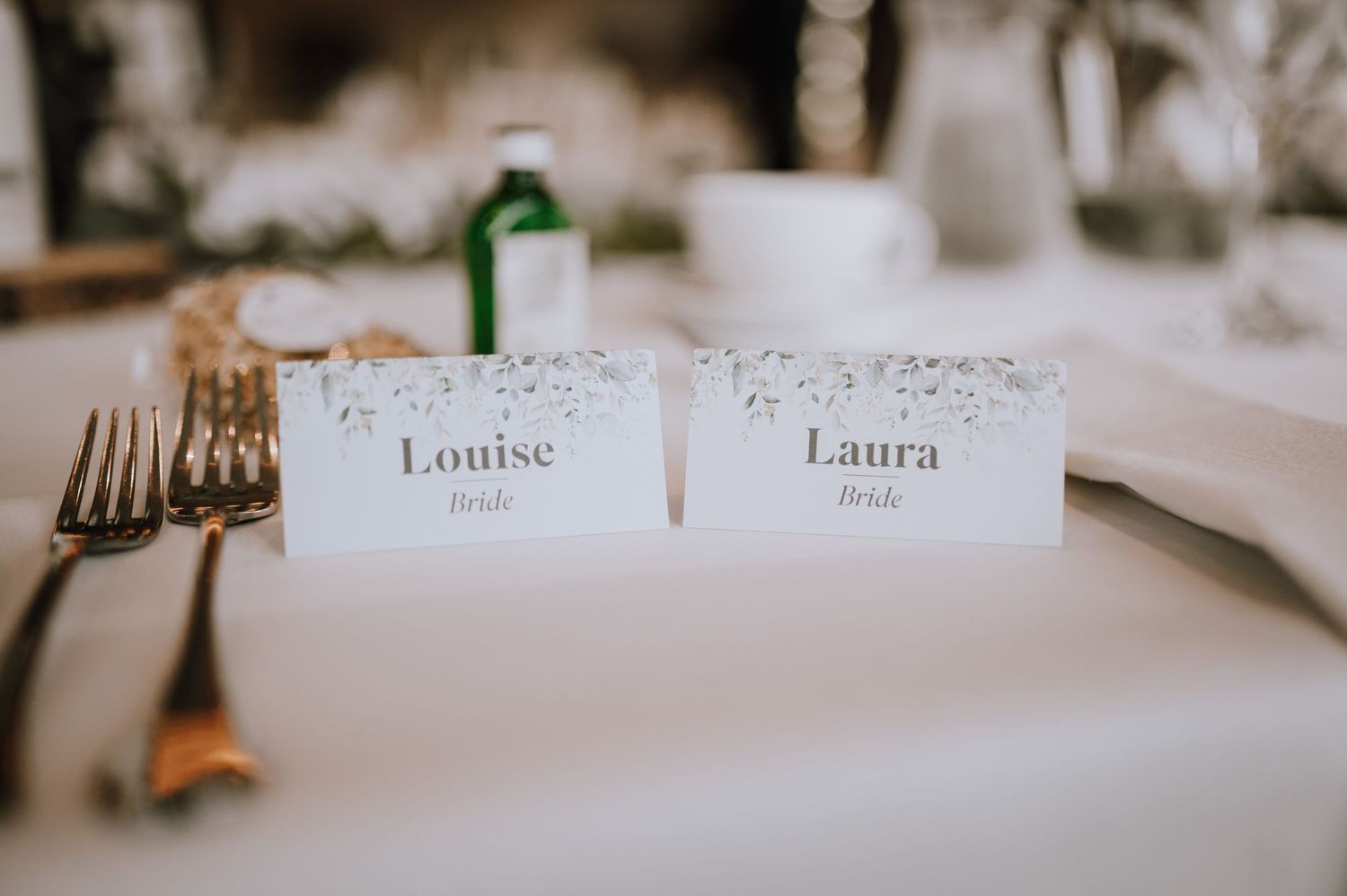Two place cards with names displayed on an elegant white tablecloth setting.