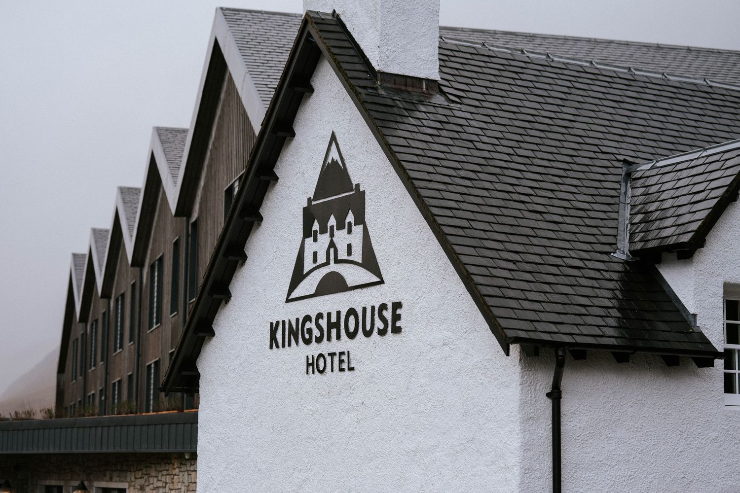 Exterior view of Kingshouse Hotel with distinctive white walls and peaked roofline against cloudy sky.