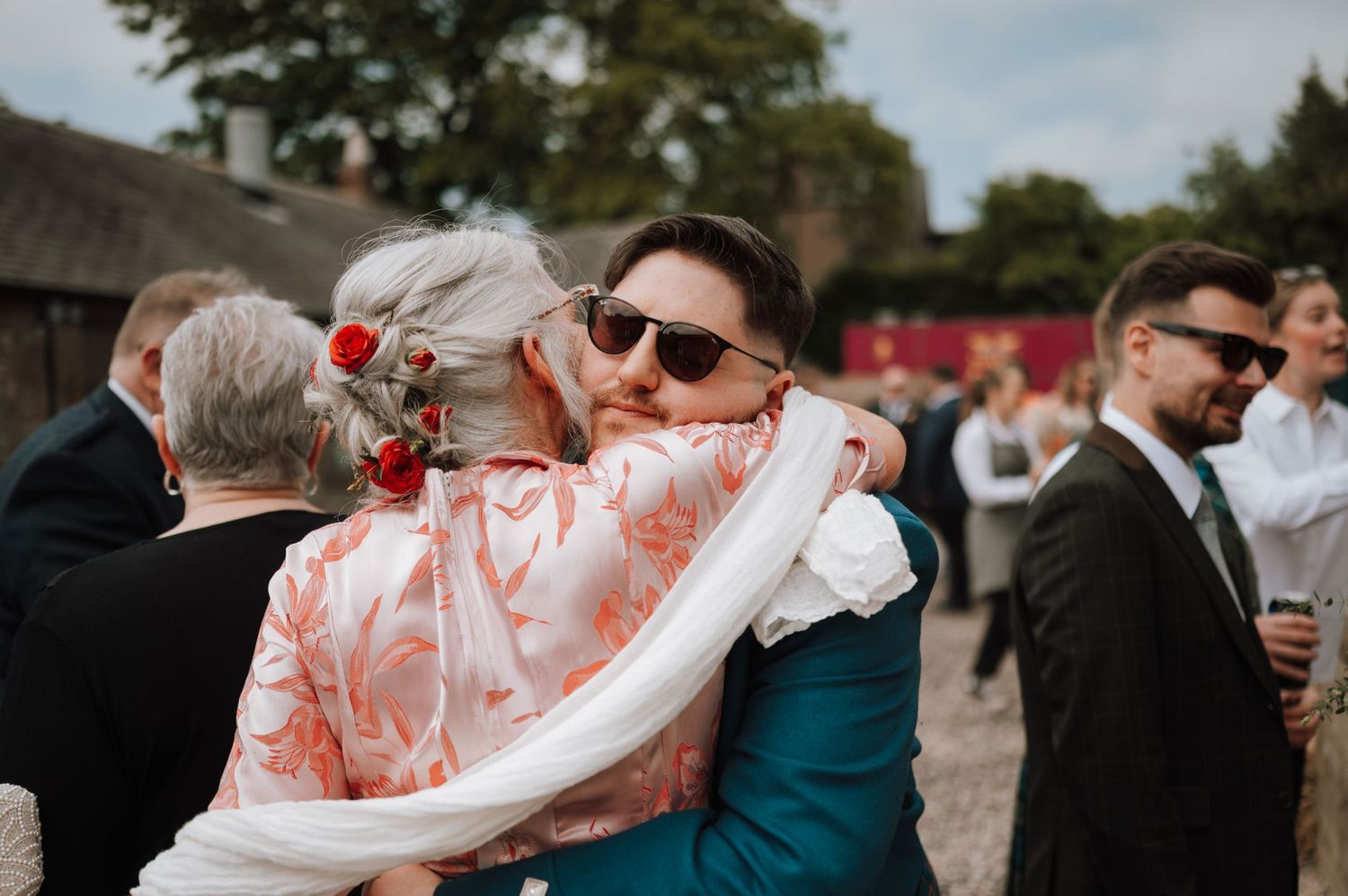 Guests embrace during outdoor wedding celebrations near a rustic barn.