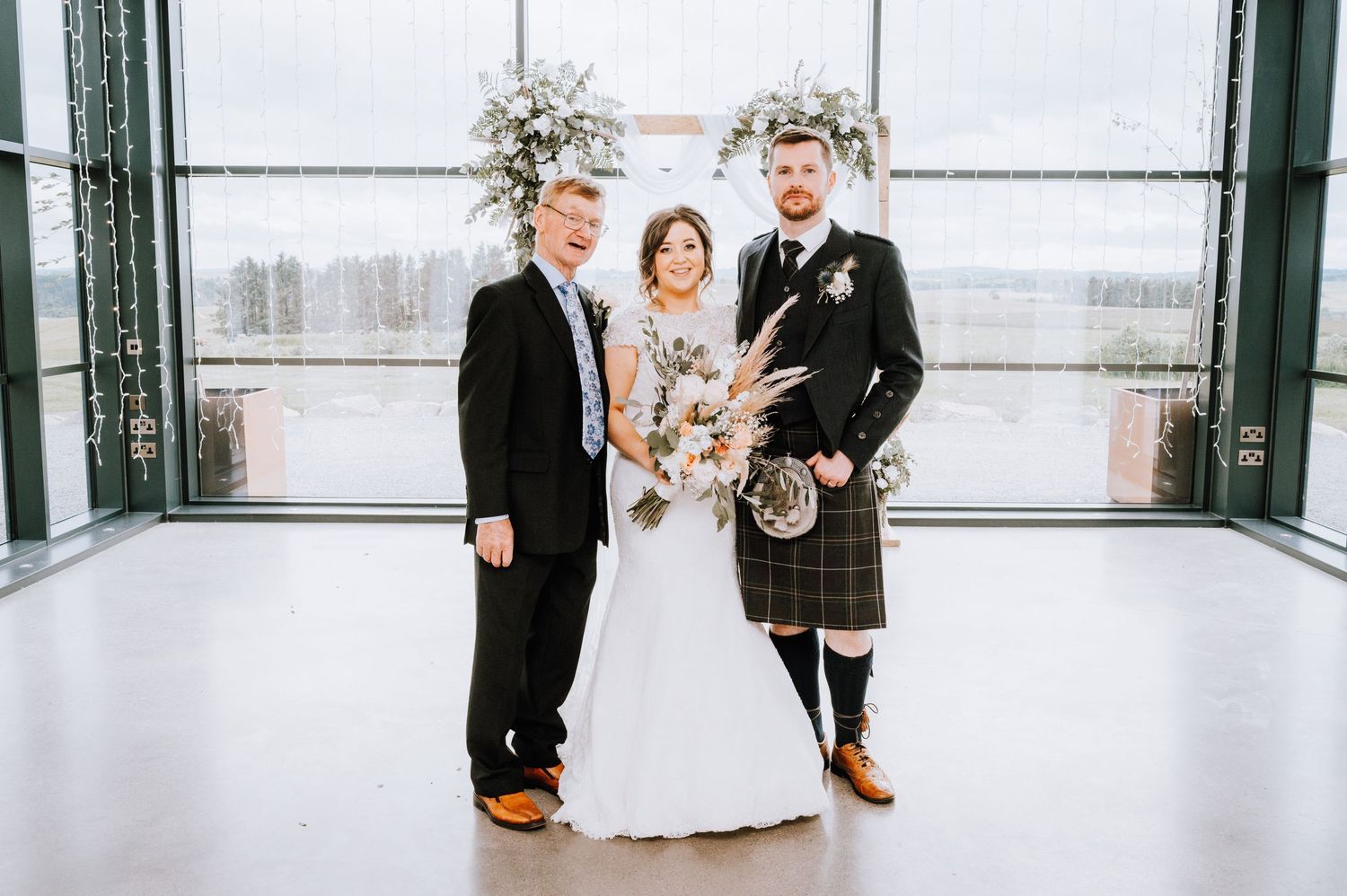 Three person wedding portrait with groom in traditional Scottish kilt in modern venue.