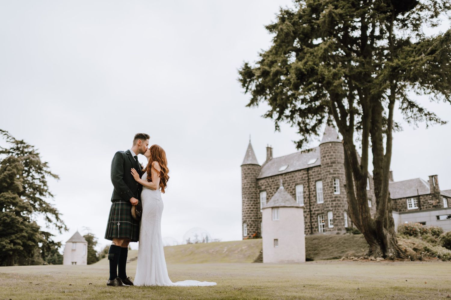 A couple poses for their wedding photos with a majestic Scottish castle in the background.