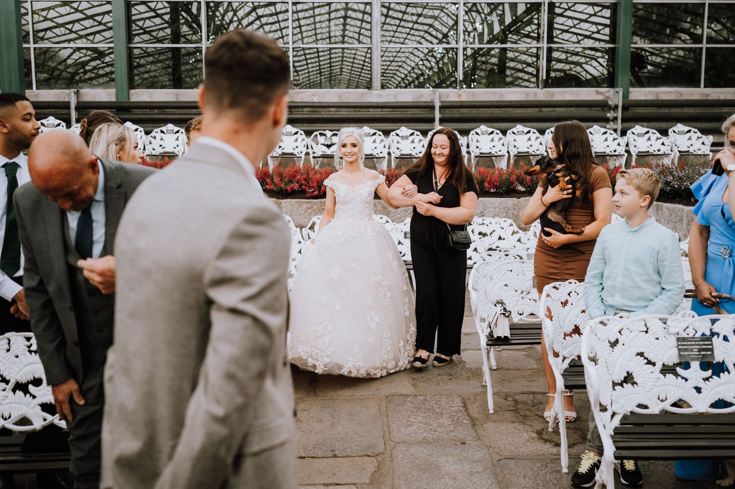 A greenhouse wedding ceremony with white chairs and guests gathering.