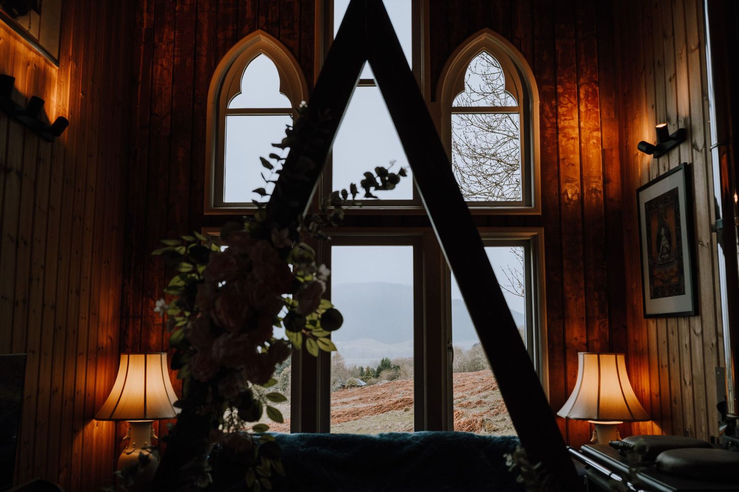 Gothic arched windows in wood-paneled room with table lamps creating cozy ambiance.