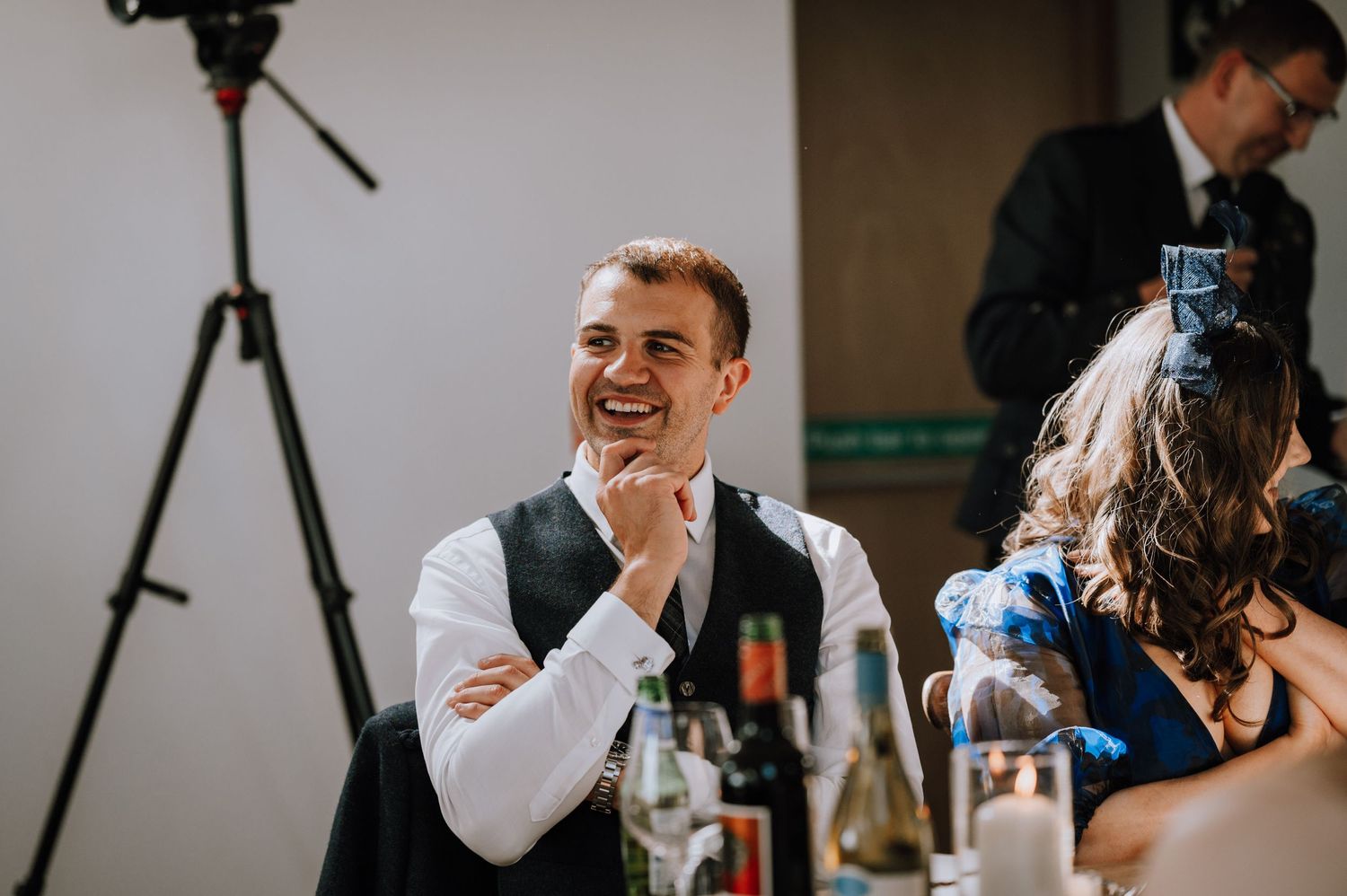 A guest laughing with joy during a wedding reception with a tripod visible in the background.