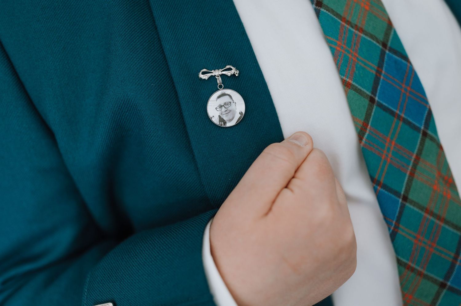 Close-up detail of a green jacket with a decorative pin and tartan tie.