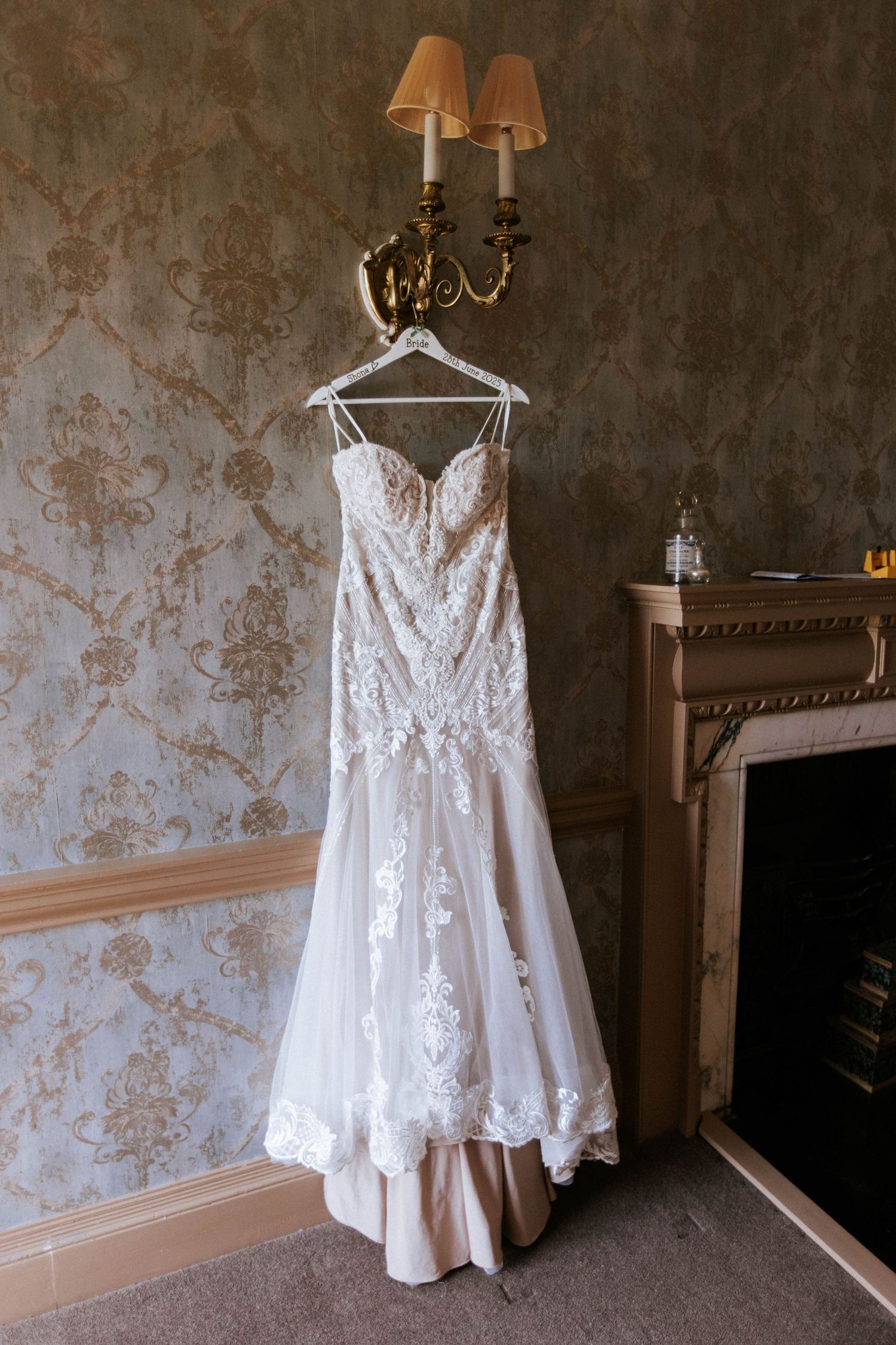 Fasque Castle Wedding Photography. An ornate white wedding dress displays intricate lace details while hanging in a vintage-style room.
