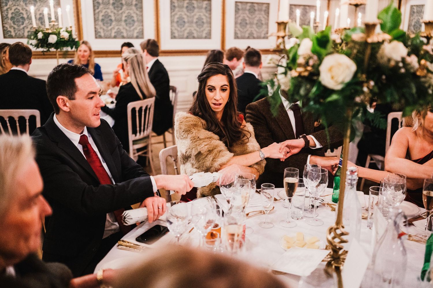Formal dinner guests seated at an elegant reception table with floral centerpieces and candlelight.