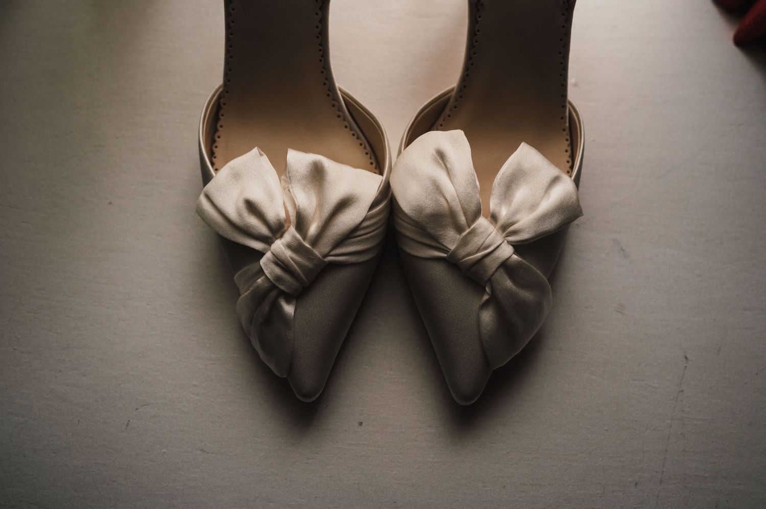 Elegant white bridal shoes with bow details photographed from above.