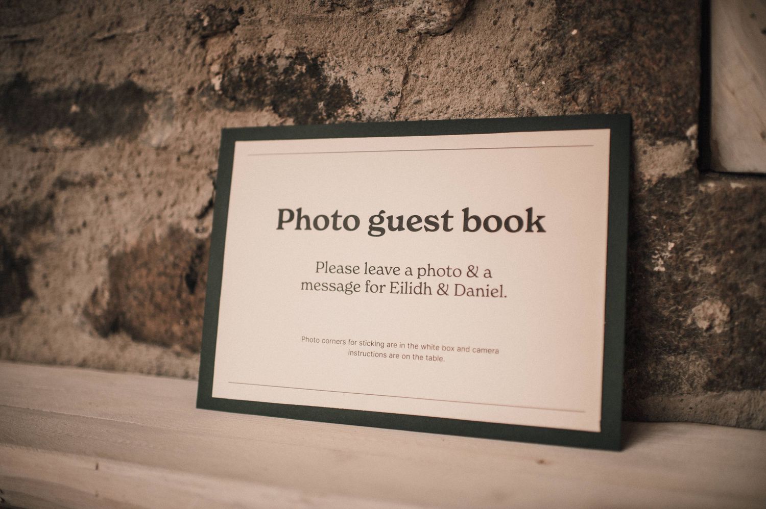 Wedding guest book sign in black frame displayed against textured stone wall.