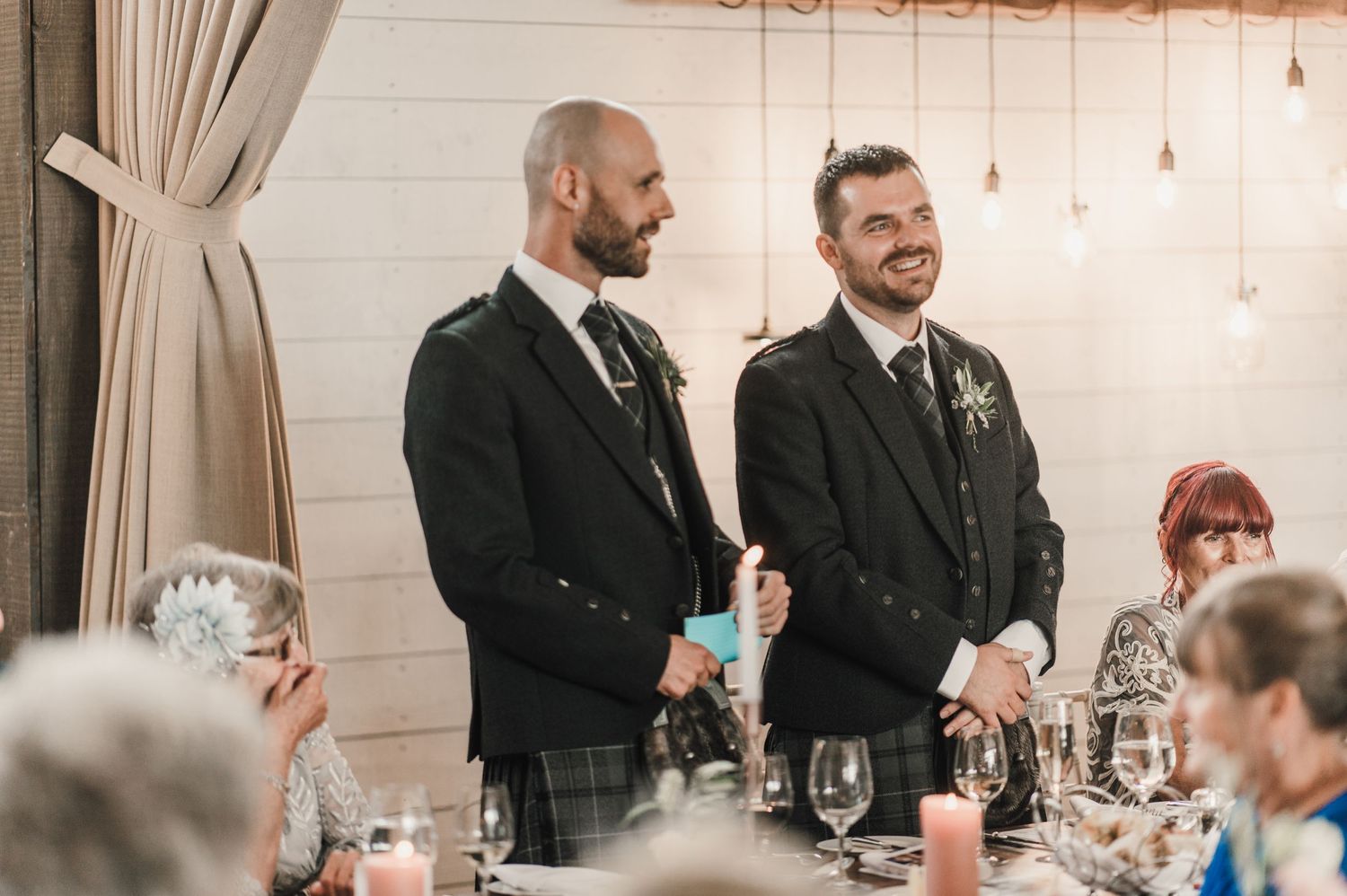 Two people in formal attire stand and share a moment during a wedding reception.