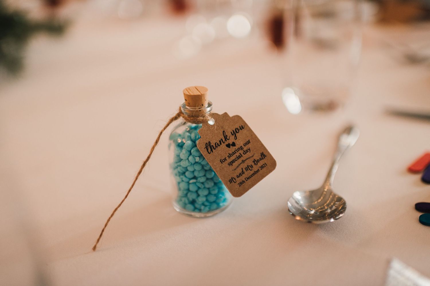 Small glass bottle with blue crystals and a handwritten tag tied with twine as a wedding favor.
