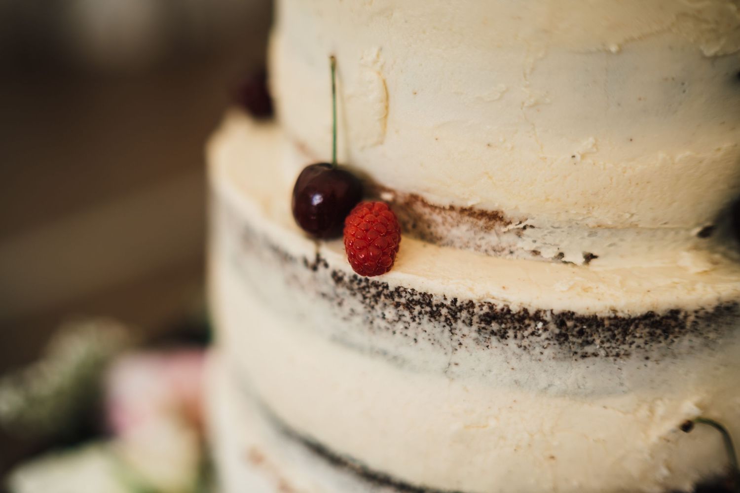 Close-up detail of a white wedding cake decorated with fresh berries and dark crumbs.