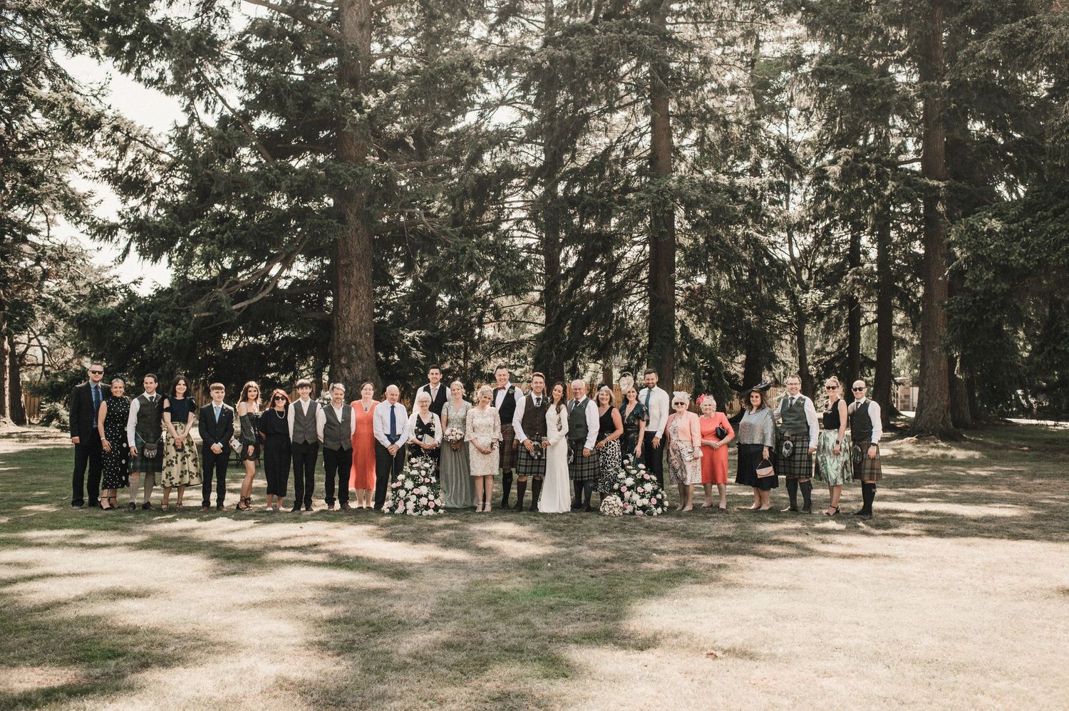 Large wedding party group photo taken in a scenic forest setting.