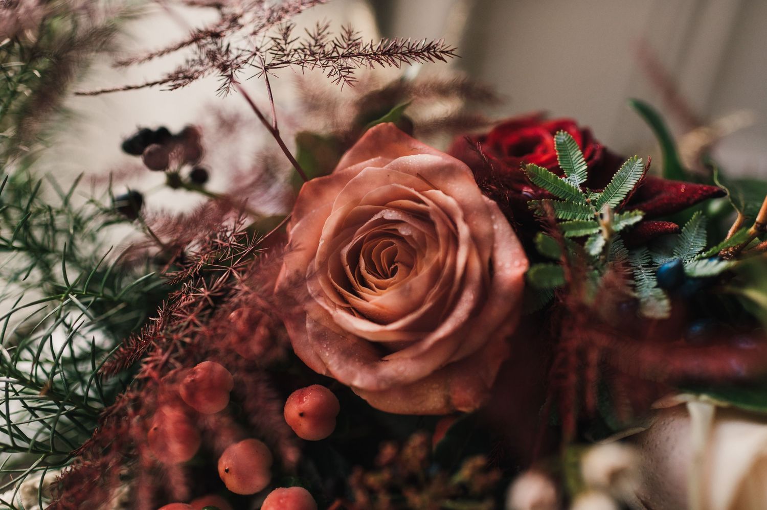 Close-up of a romantic floral arrangement featuring a peach rose and deep red accents.