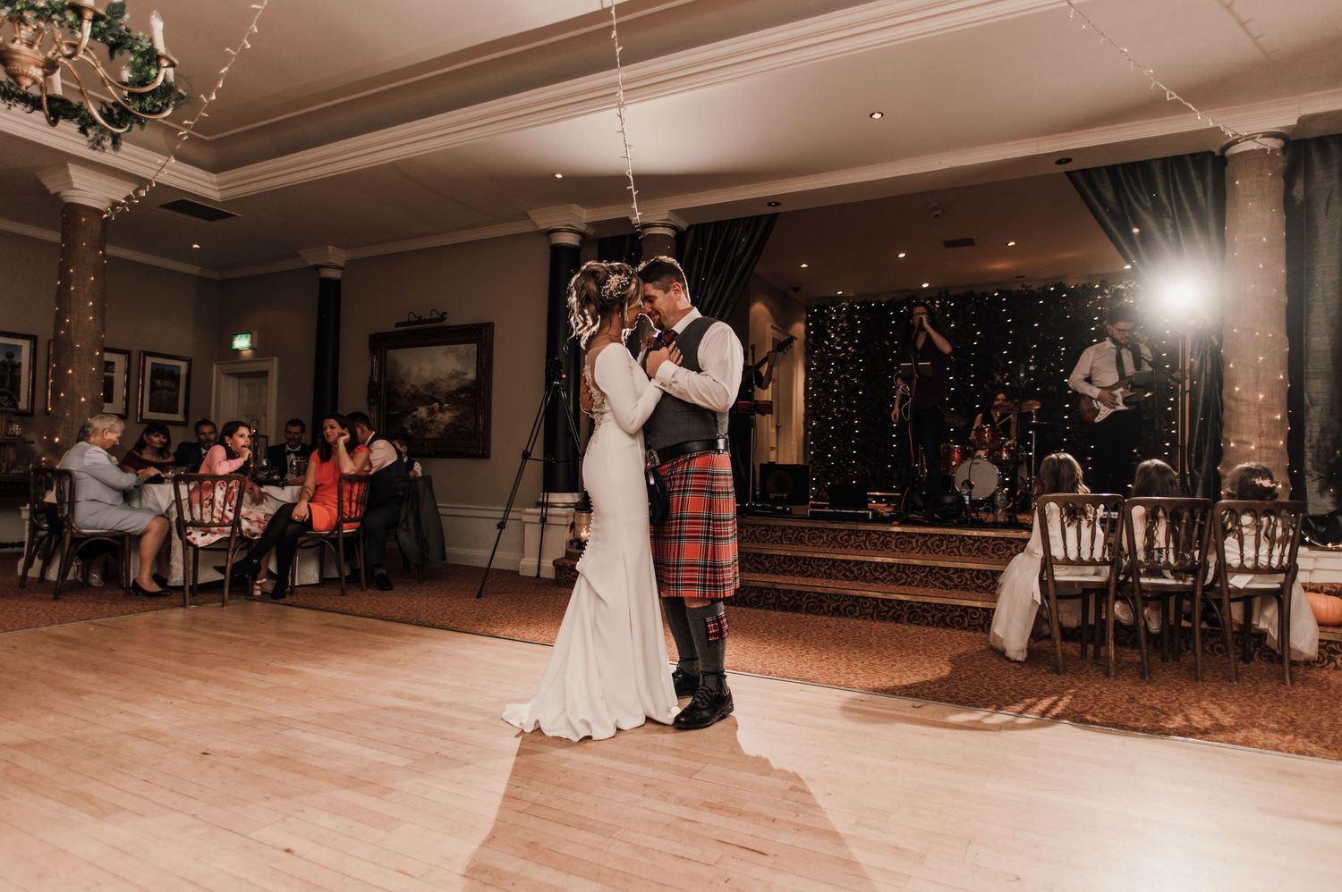 An elegant ballroom first dance at a wedding with string lights and classical columns in the background.