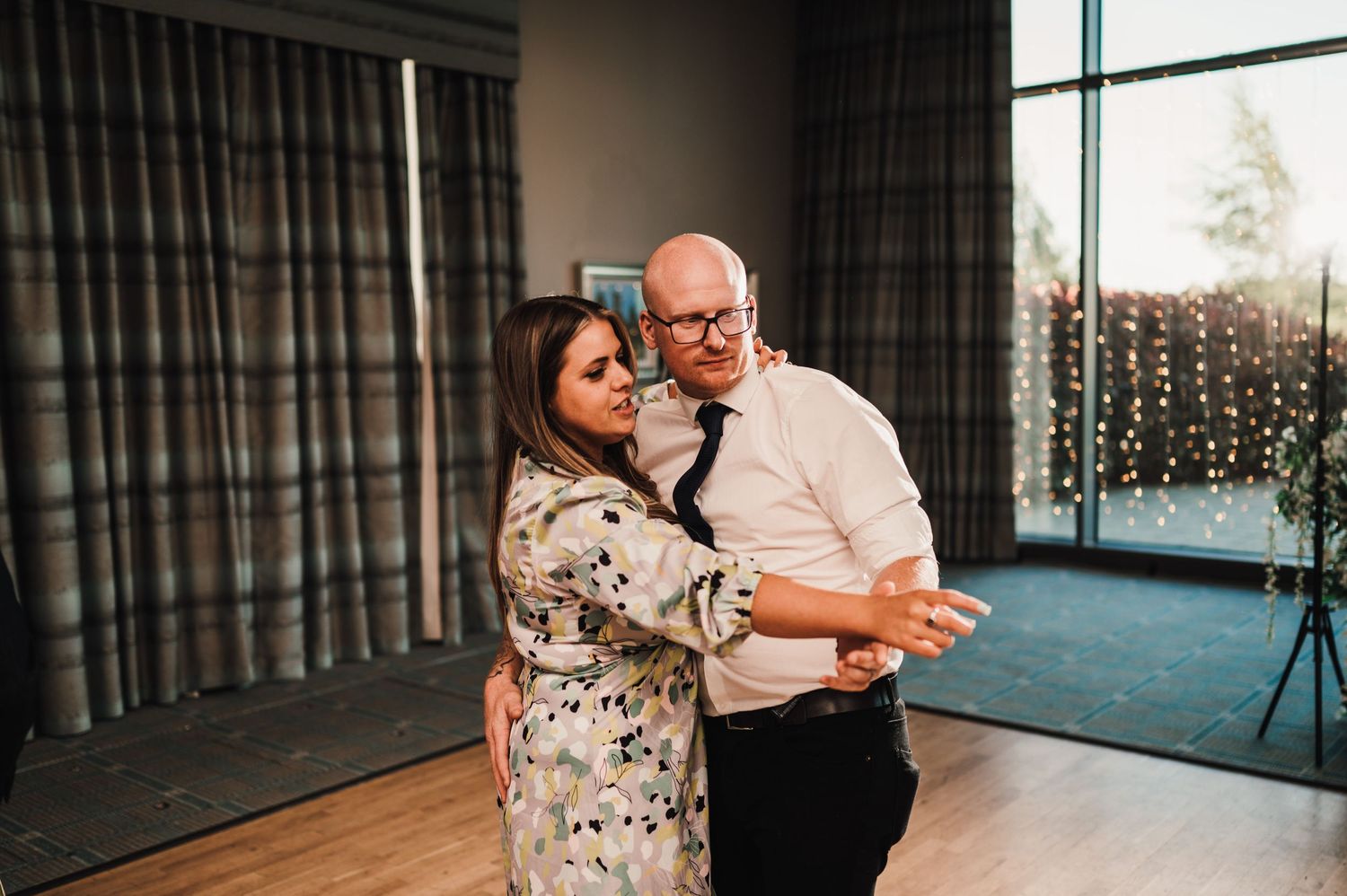 Couple dancing together at wedding reception with floor-to-ceiling windows and blue carpet.
