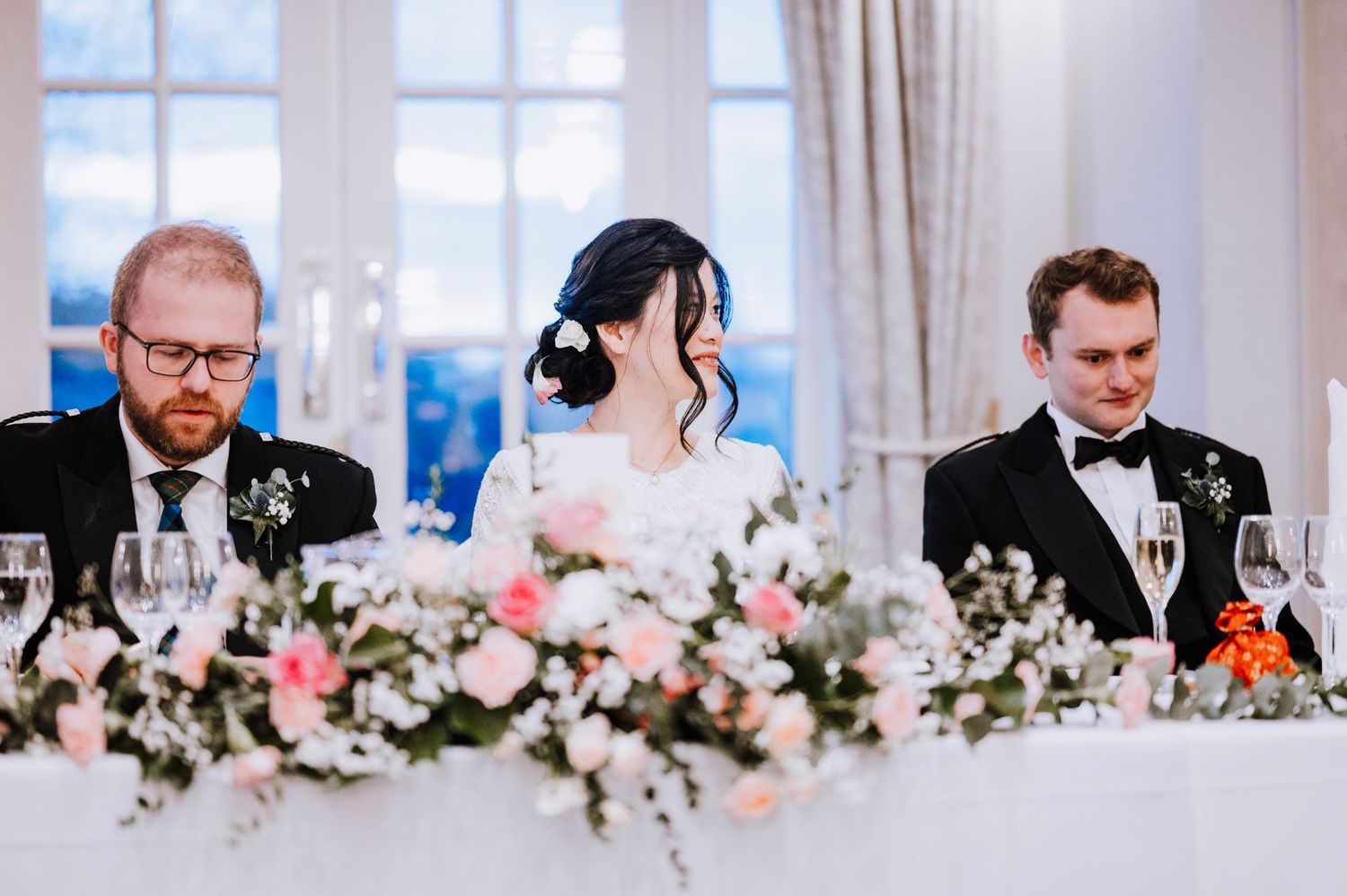 Head table at wedding reception decorated with pink and white floral arrangements.