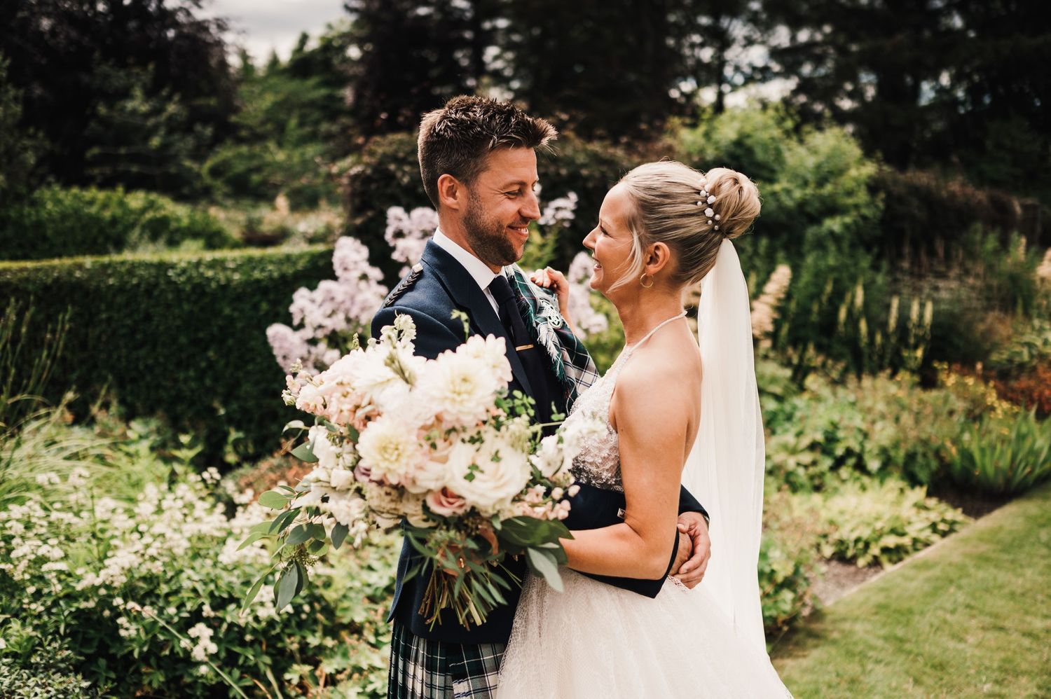 Newlyweds share an intimate moment in a lush garden setting with beautiful white floral bouquet.