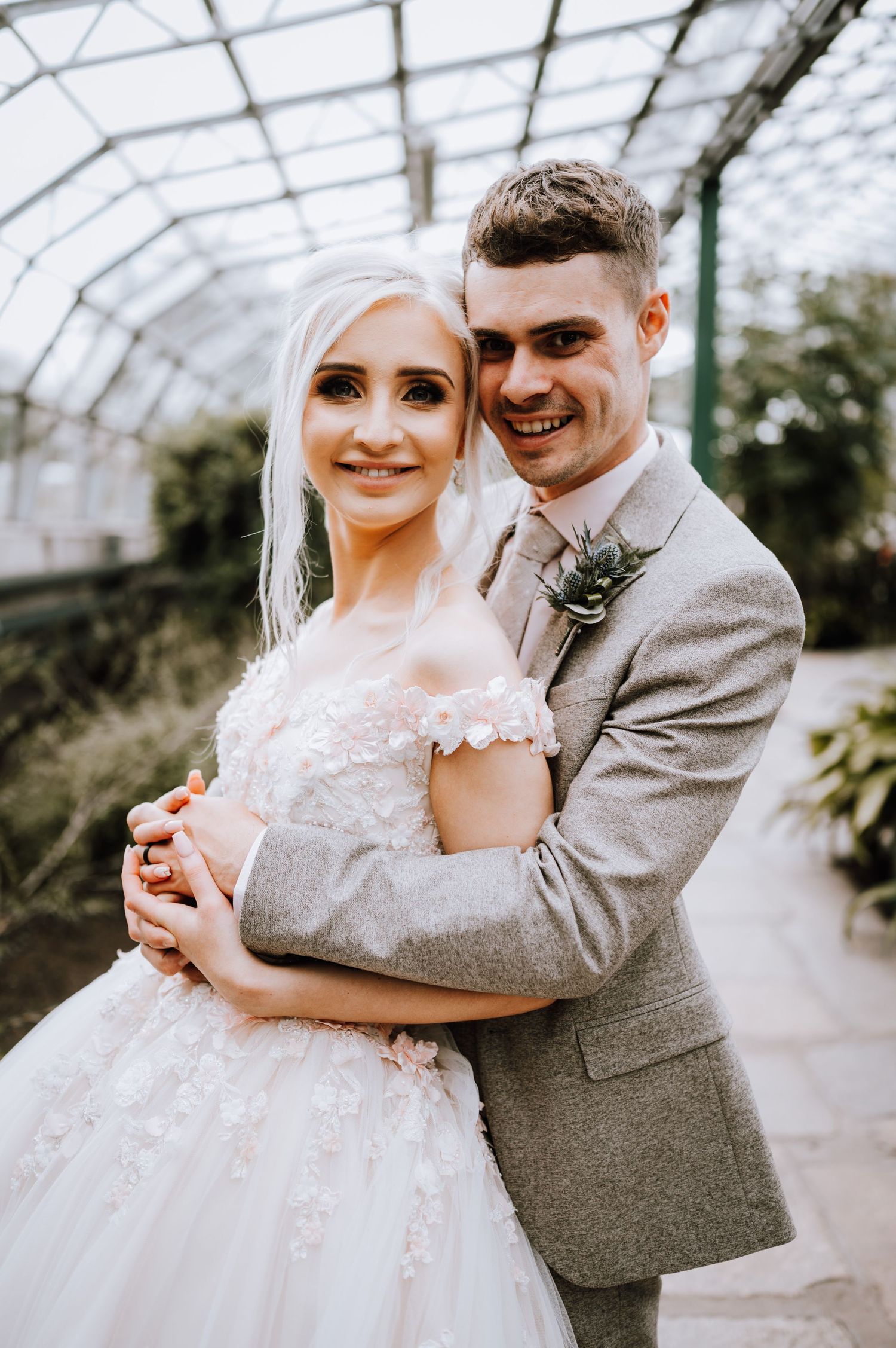 A joyful wedding portrait showcasing a couple in a greenhouse with glass ceiling overhead.