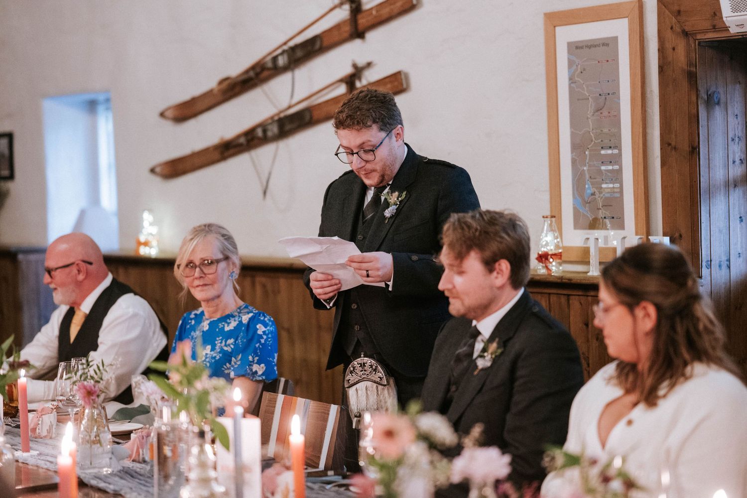 Long dining table set for wedding reception with candles and rustic decor in stone-walled venue.