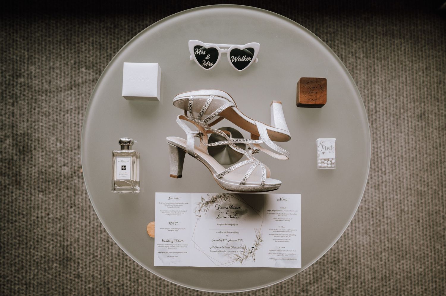 Wedding accessories including white heels, perfume, and jewelry arranged on a circular surface.