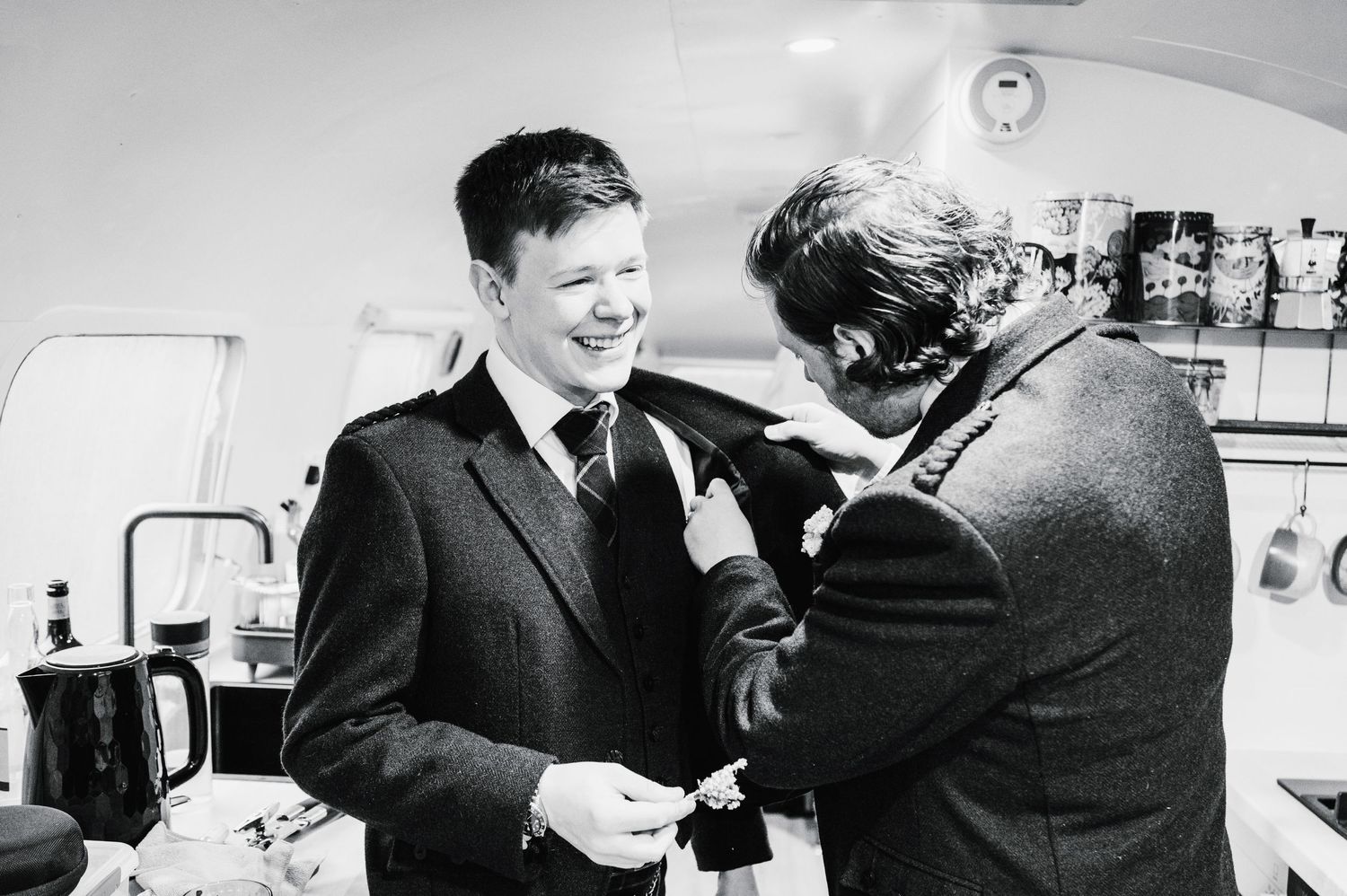 Two people share a lighthearted moment during wedding preparations in black and white photography.