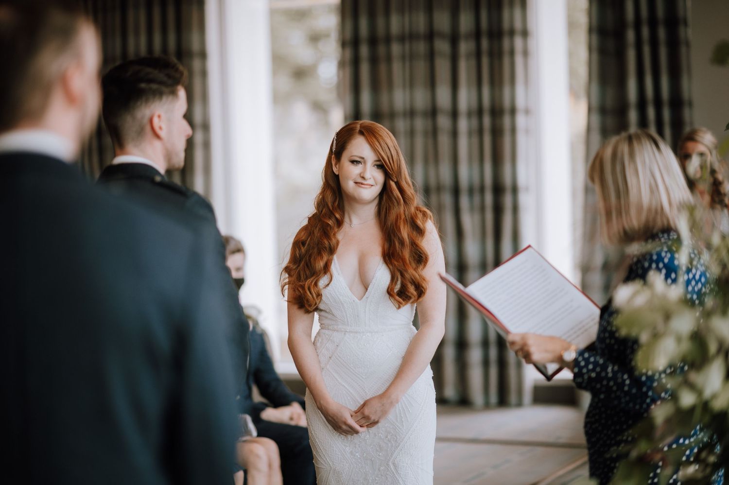 A couple exchanges vows during an indoor wedding ceremony while guests look on.