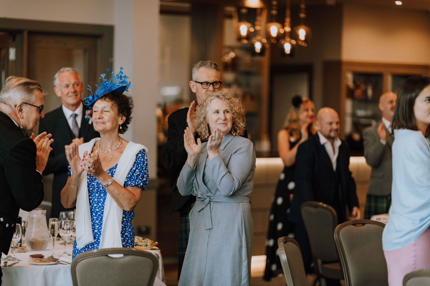 Wedding guests in formal attire applauding during an emotional moment at the reception.