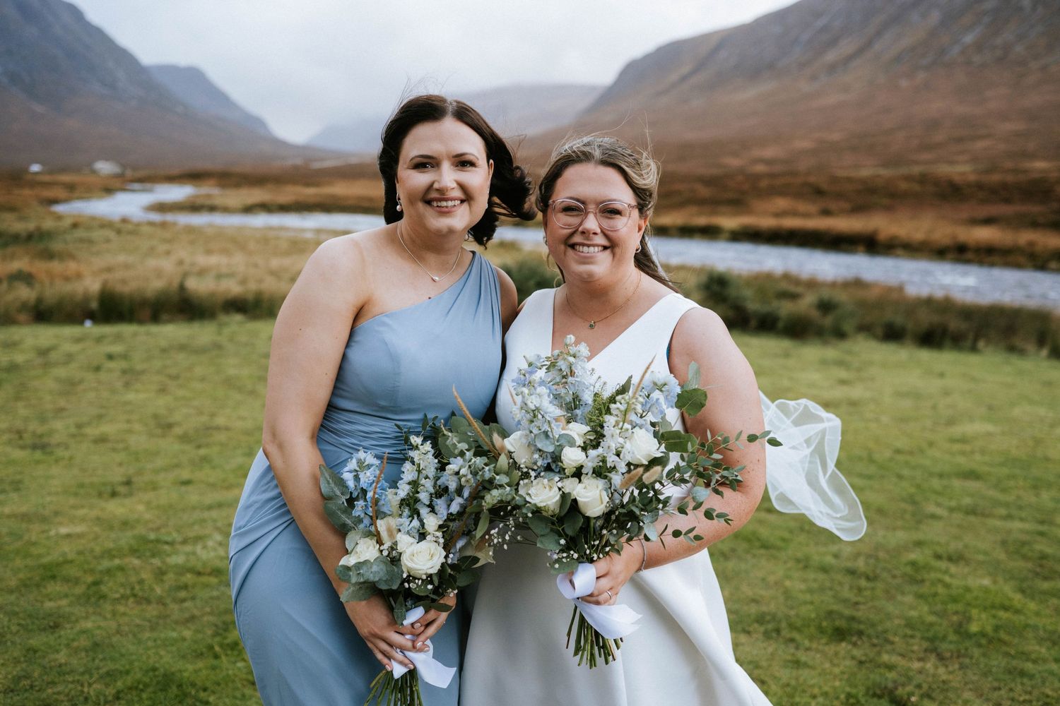 Wedding party with blue and white floral bouquets poses in front of mountain vista.