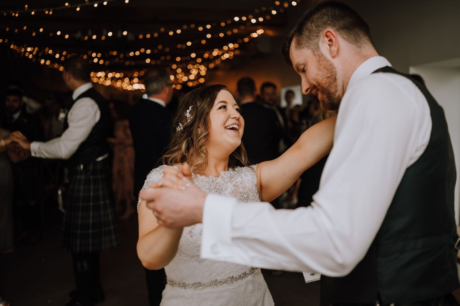 Newlyweds share a joyful dance together at their wedding reception under warm lighting.